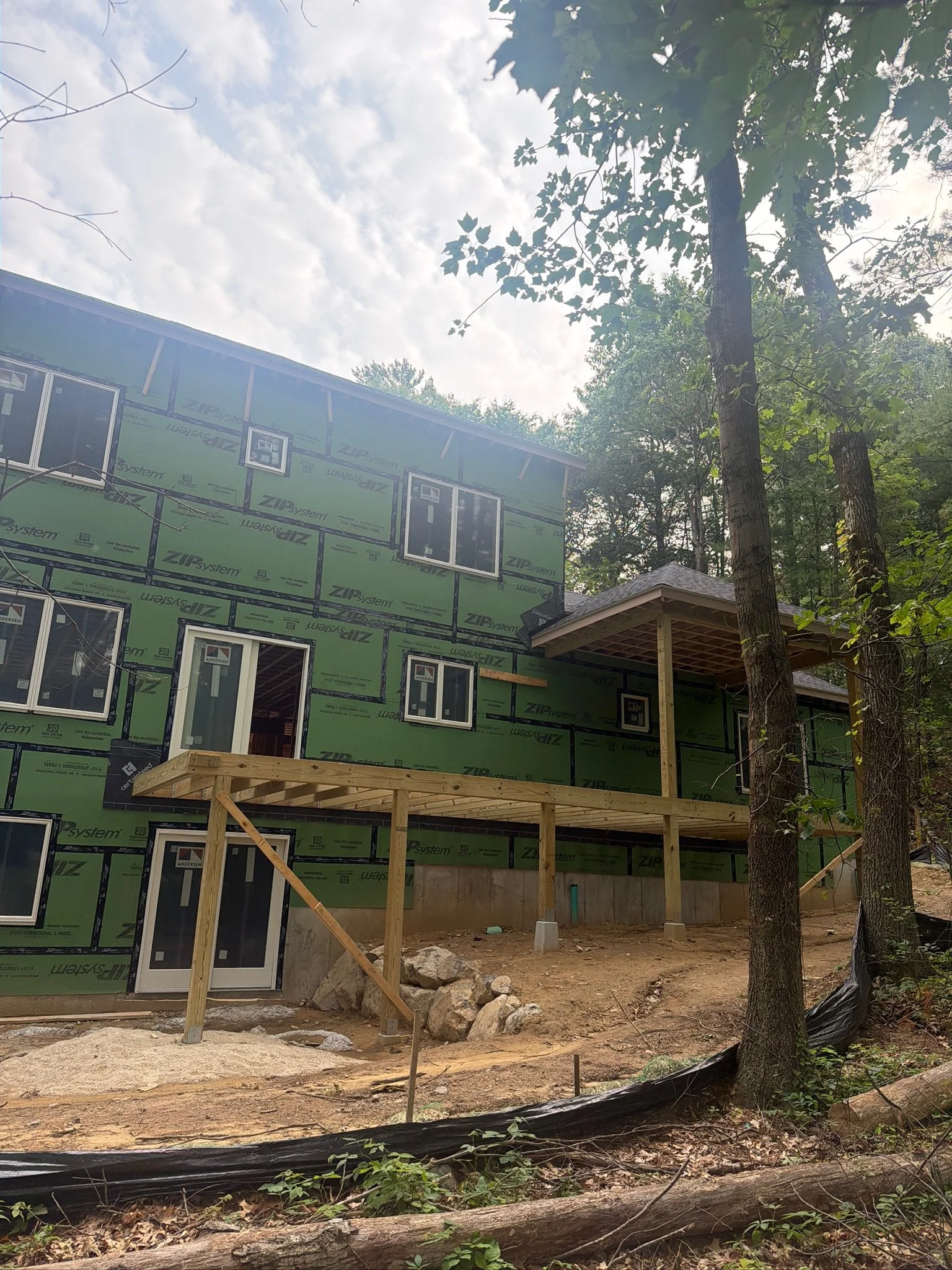 Rear elevation framing of a custom multi-story home with ZIP System sheathing and deck support beams set against a wooded backdrop.