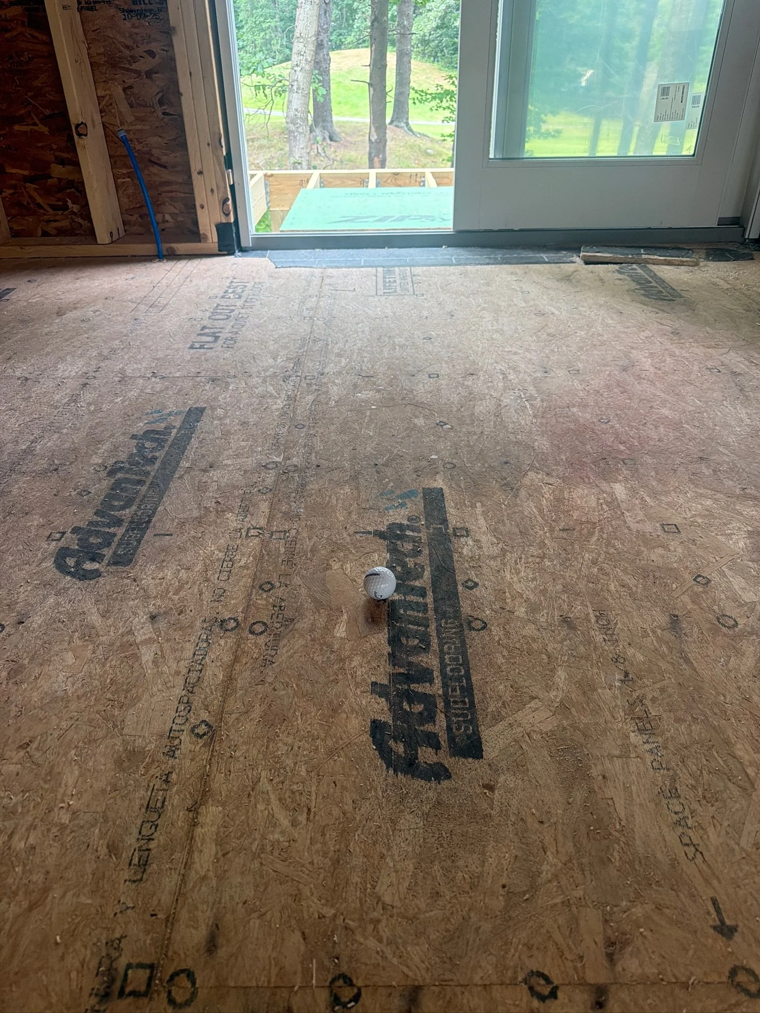 Custom home construction site featuring sub-flooring and glass sliding doors overlooking scenic golf course greens.