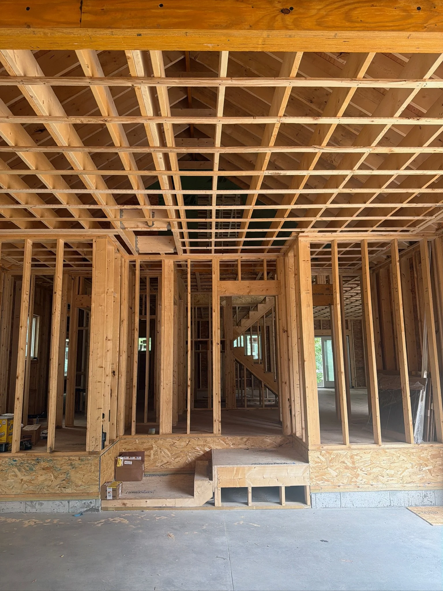 Custom home construction progress showing exposed wood wall framing, sub-flooring, and intricate ceiling joists.
