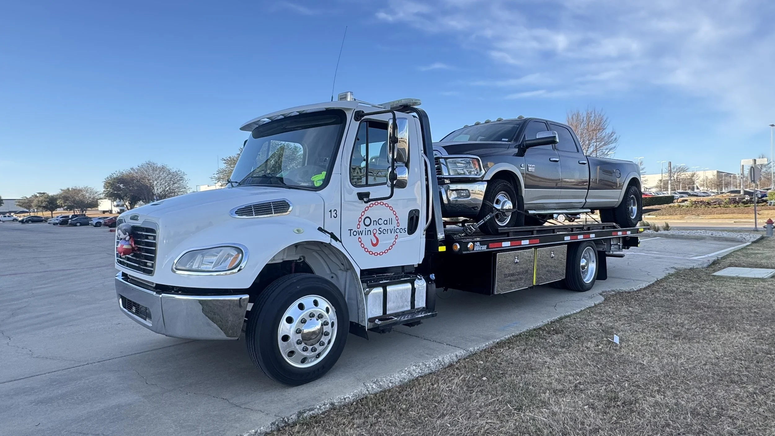 A tow truck carrying a black pickup truck in a parking lot under a clear blue sky.