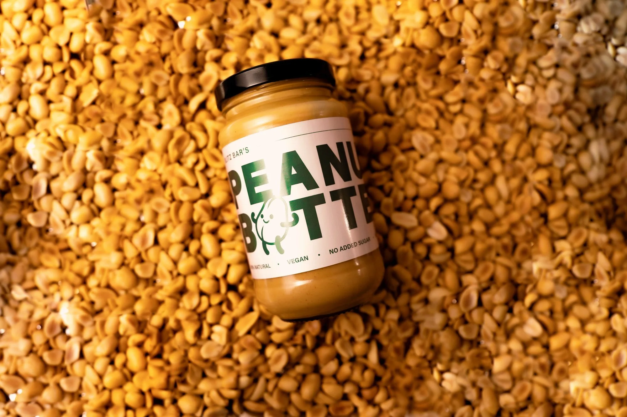 Blitz Bar crunchy peanut butter jar resting on roasted peanuts