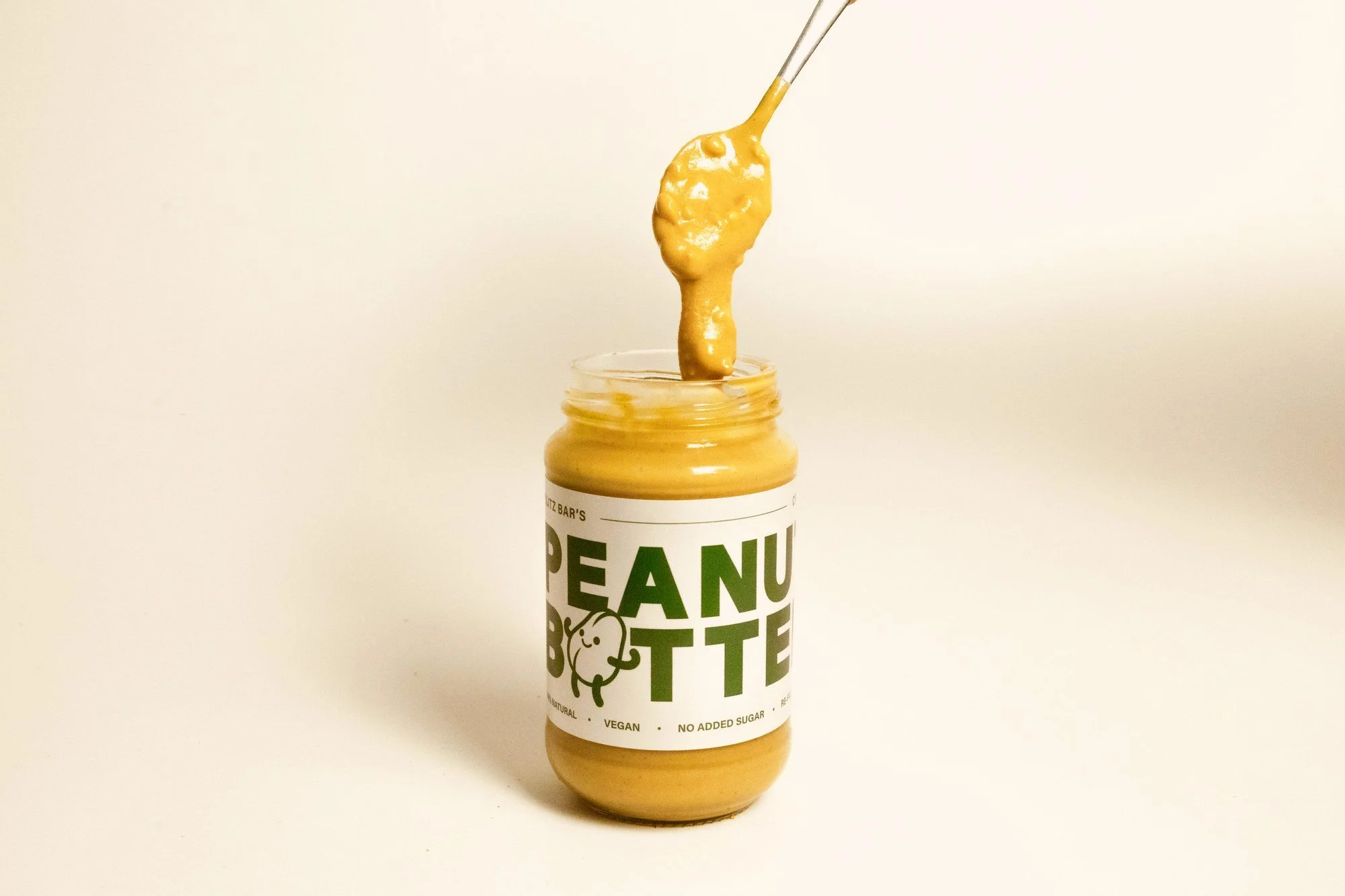 Crunchy peanut butter pouring from a spoon into a Blitz Bar jar