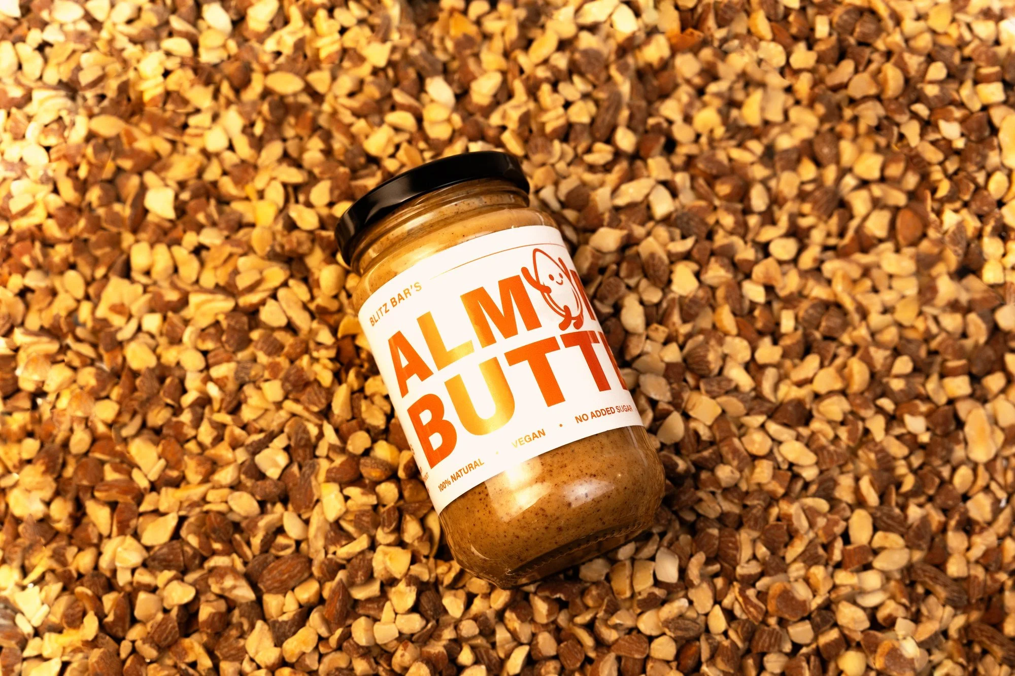 Blitz Bar almond butter jar resting on raw almonds