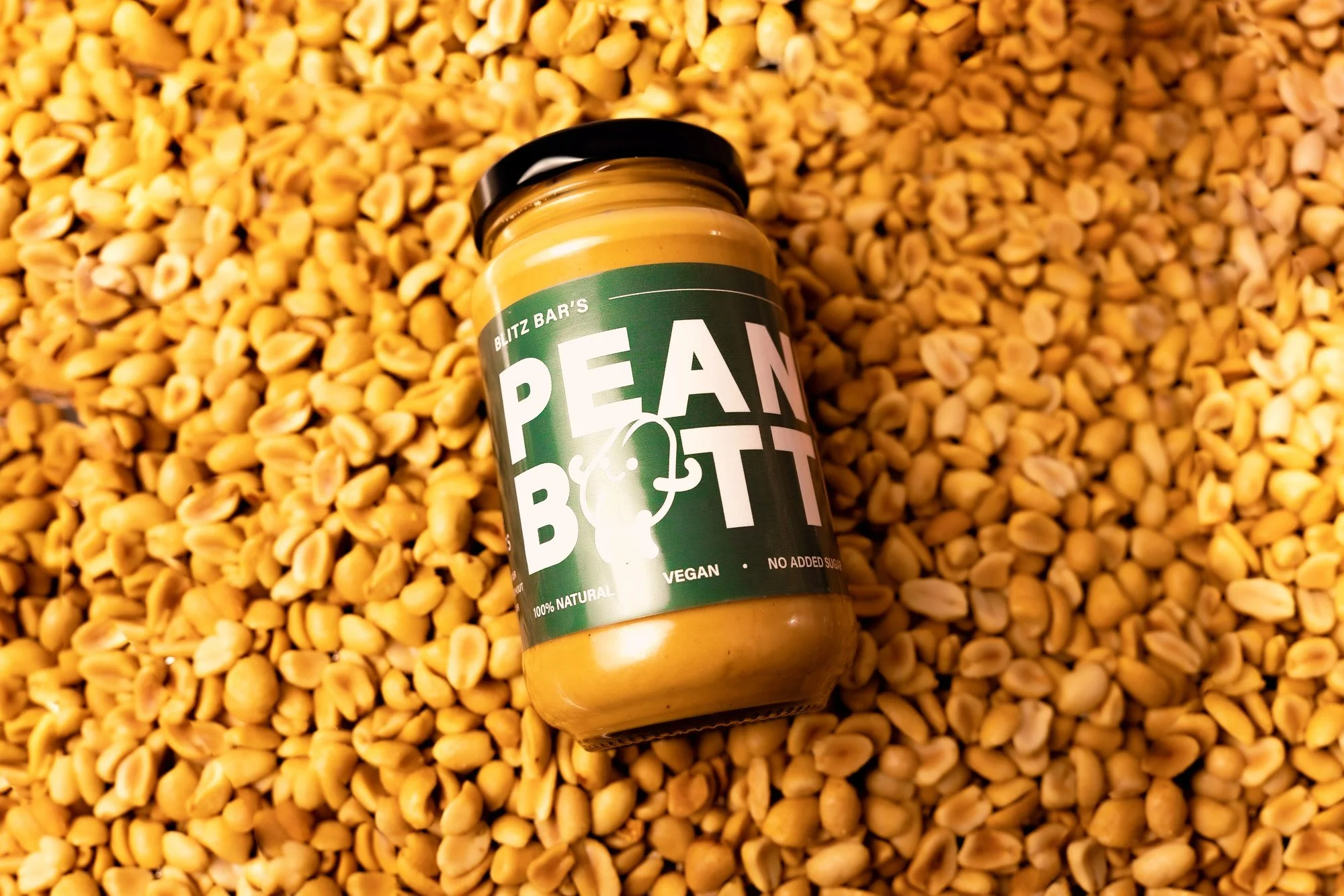 Blitz Bar smooth peanut butter jar resting on roasted peanuts