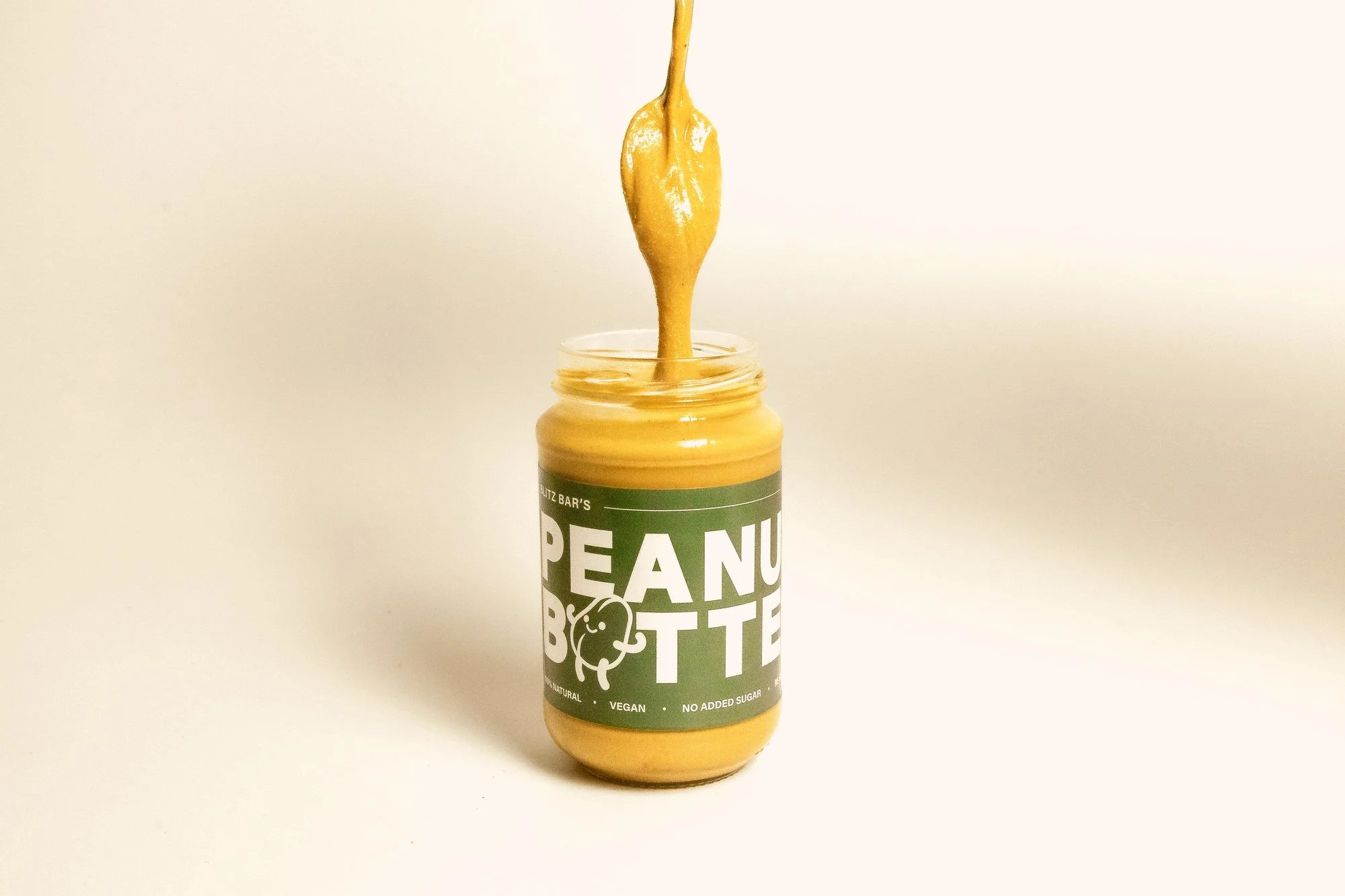 Smooth peanut butter pouring from a spoon into a Blitz Bar jar