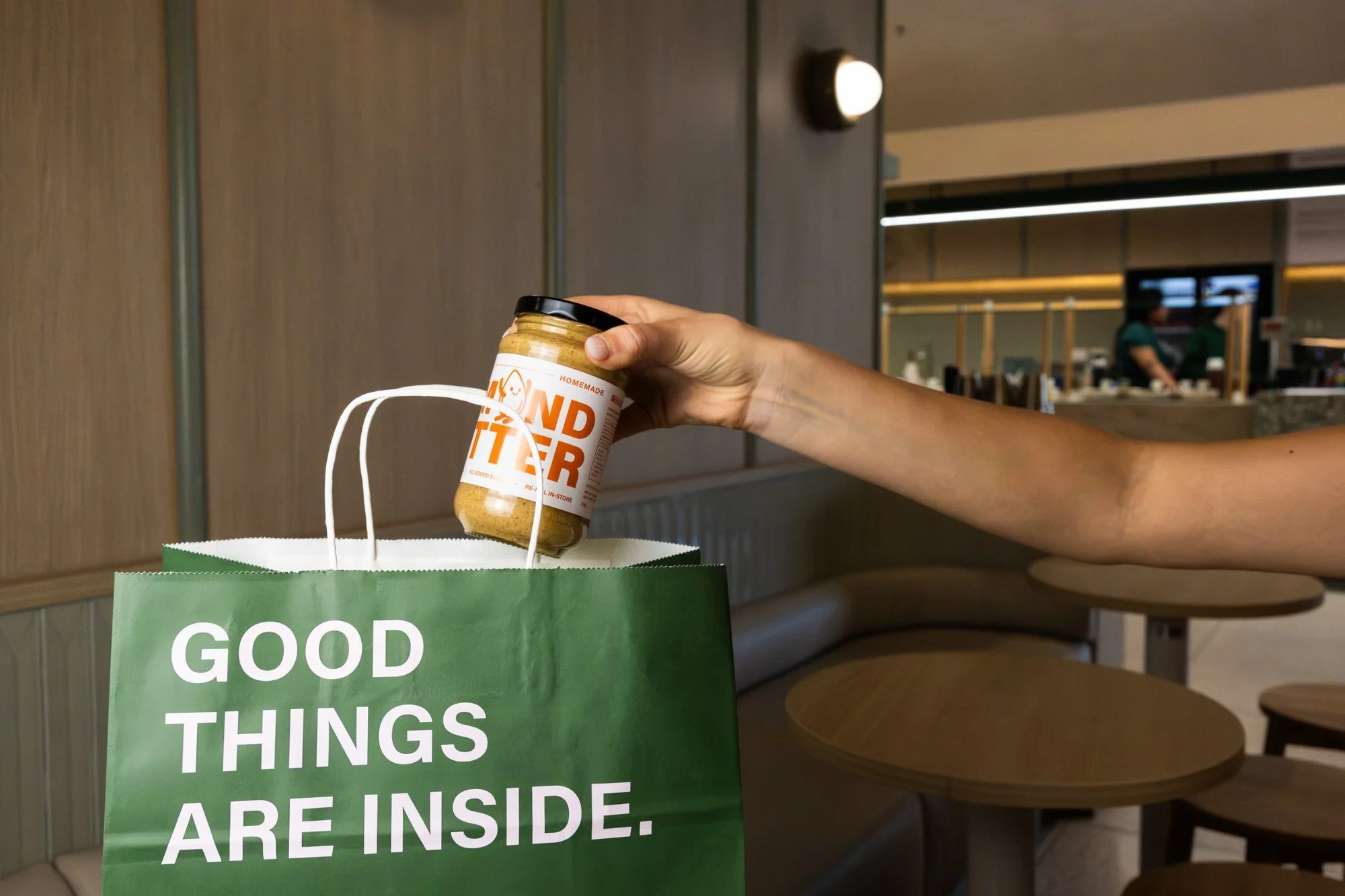 Jar of Blitz Bar almond butter being placed into a Blitz Bar takeaway bag in store