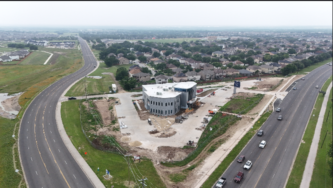 An aerial view of a construction site with a partially built modern building, surrounded by roads and residential neighborhoods.