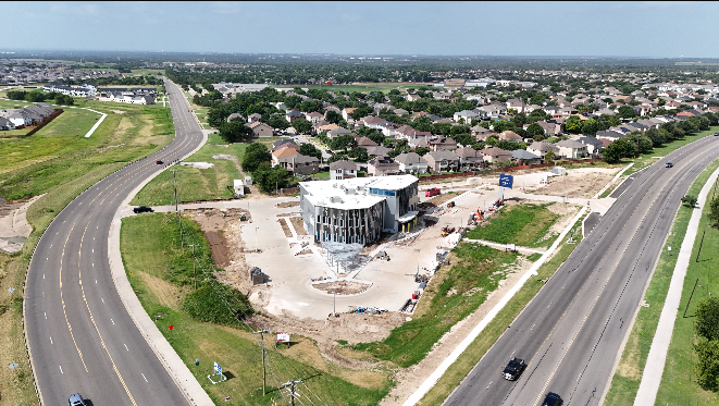 An aerial view of a construction site with a modern building in progress, surrounded by roads and residential neighborhoods.