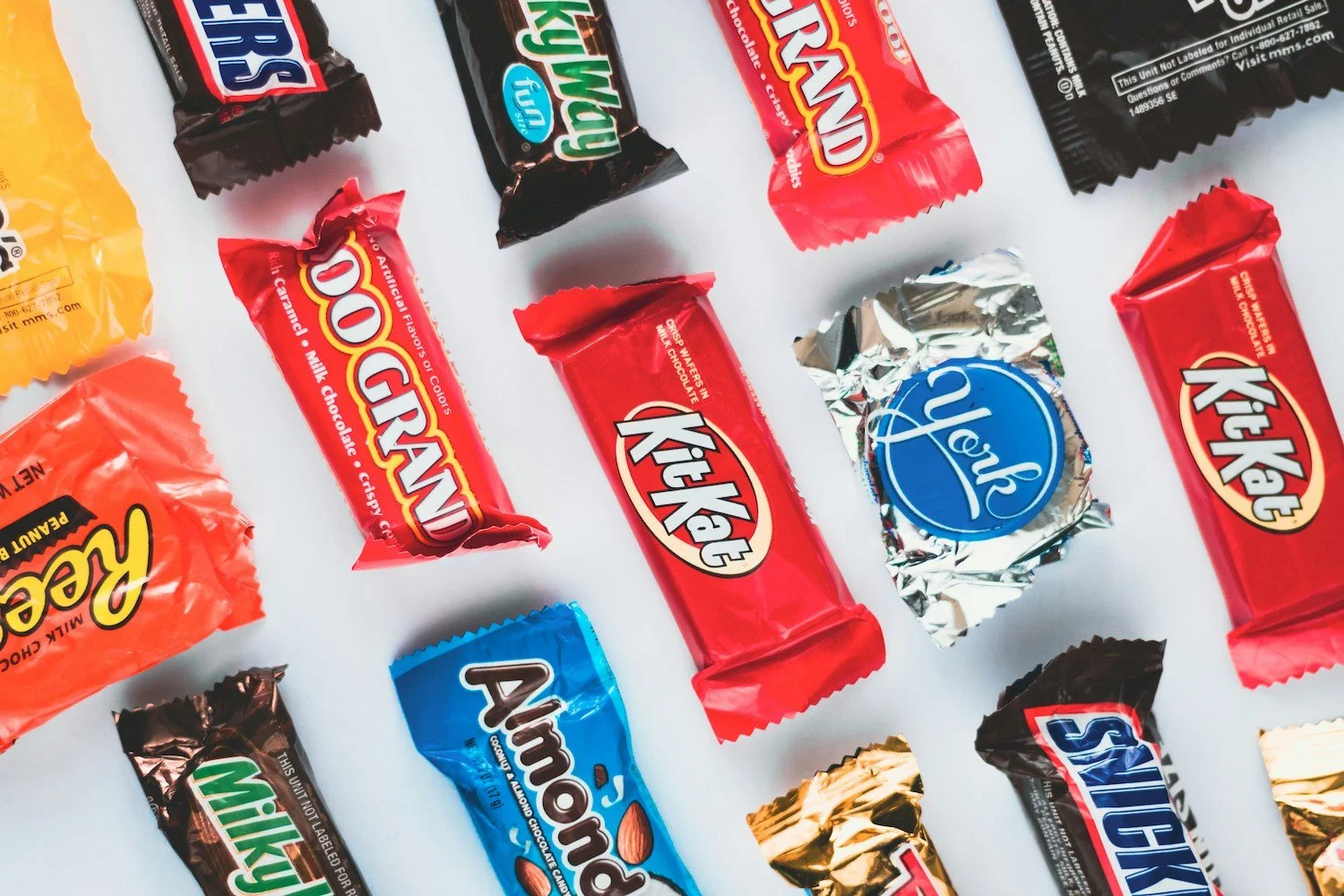 Assorted candy bars on a white surface, including Kit Kat, Snickers, Almond Joy, Reese's, and Mounds.
