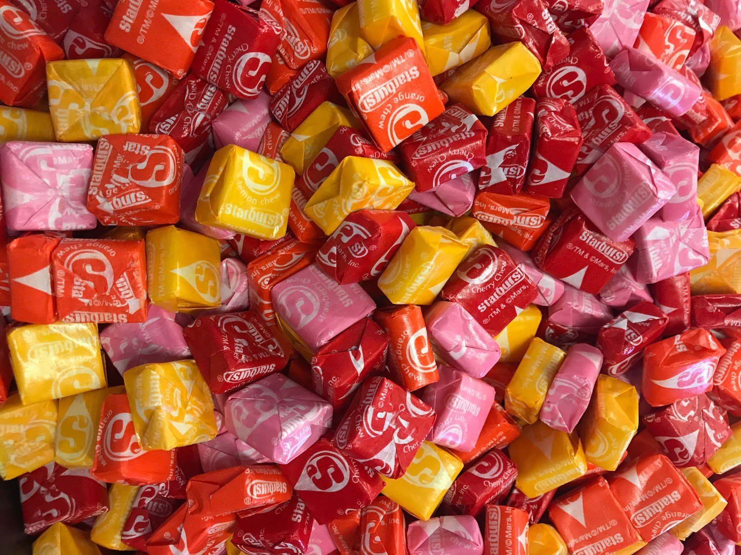 Colorful candies wrapped in pink, yellow, orange, and red wrappers, piled together.