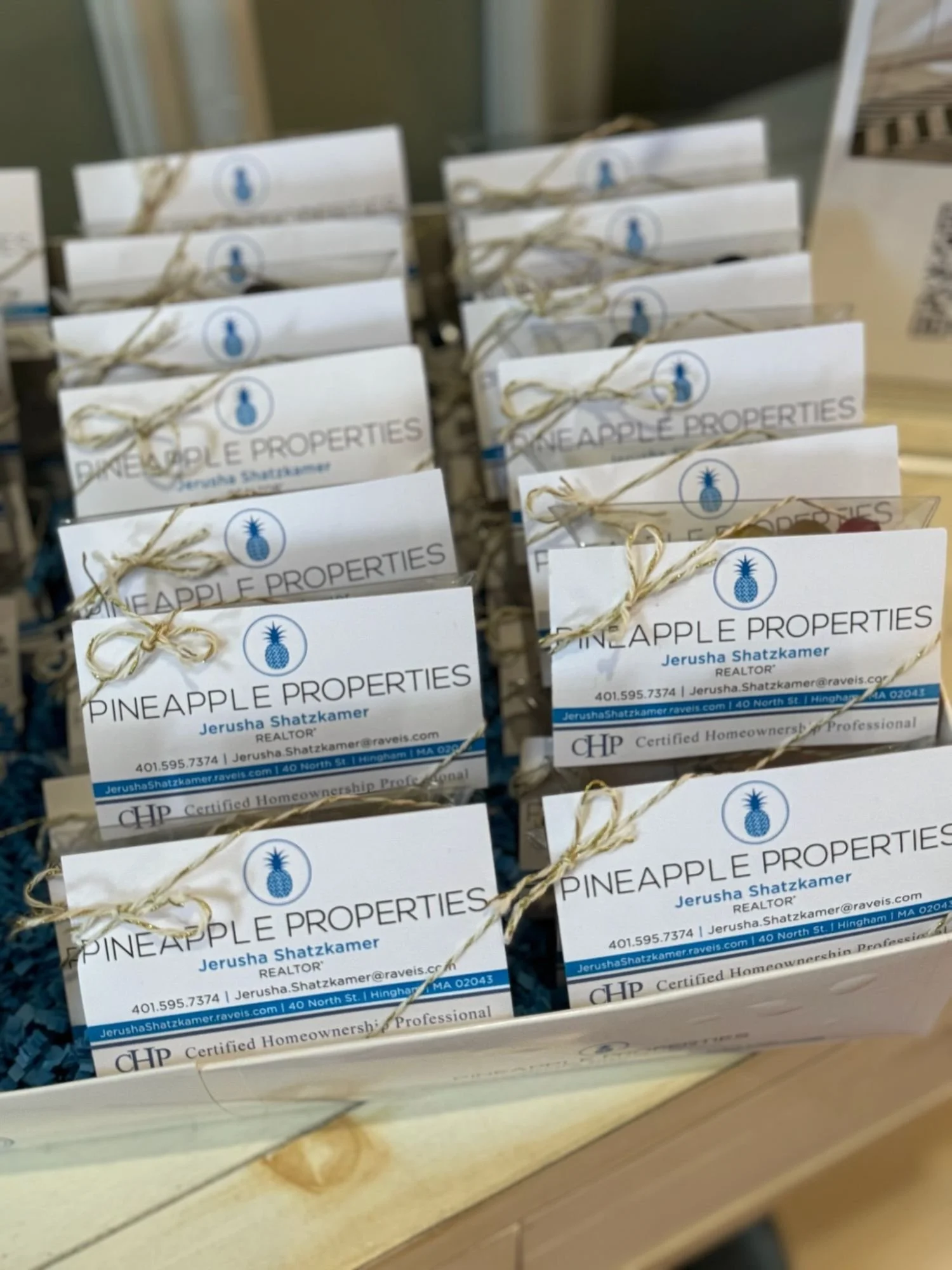 Business cards from Pineapple Properties stacked and tied with twine, featuring contact information for Jerusha Shatzkamer, a realtor.