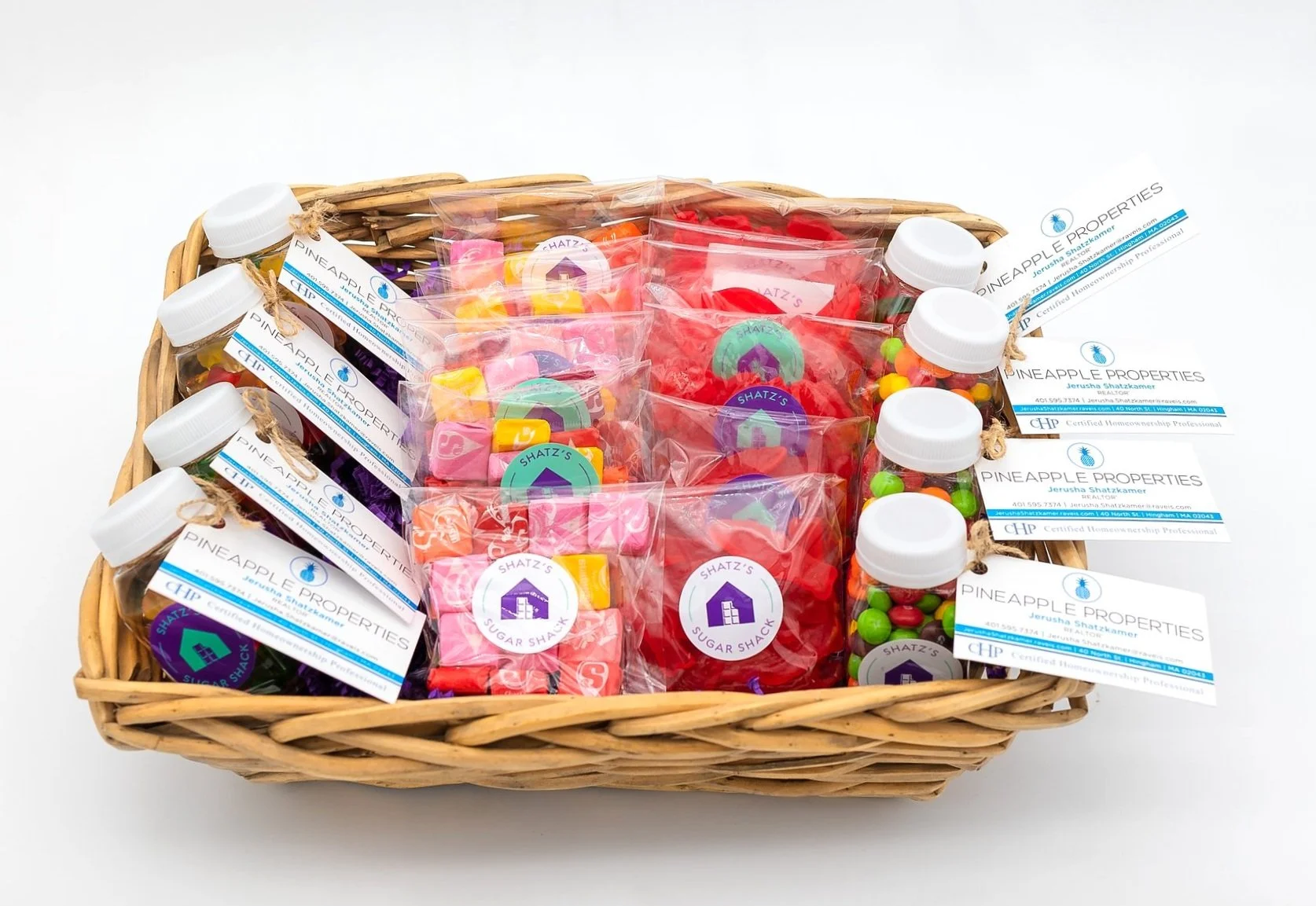 Gift basket containing jars of colorful candies, individually wrapped candies, and business cards for Pineapple Properties with real estate contact information.