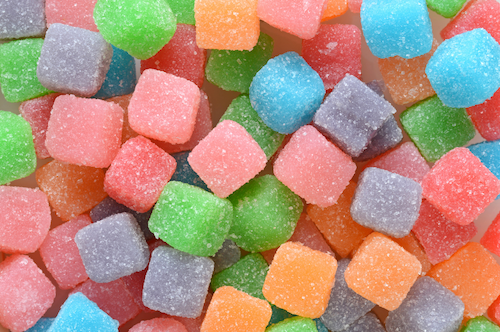 Close-up of colorful sugar-coated gumdrops or jelly candies in various colors including green, pink, orange, blue, purple, and gray.