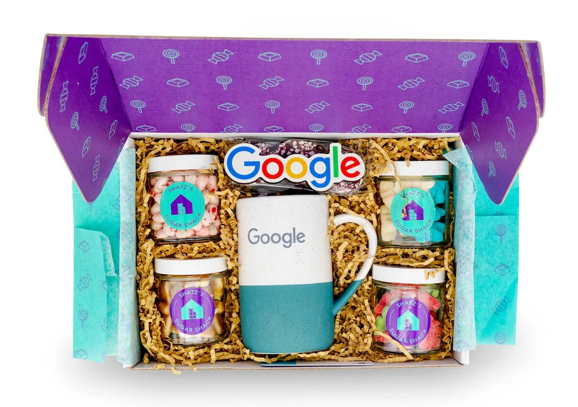 Gift set with a Google-themed mug and small jars of colorful candies labeled 'Sugar Shack' inside a purple and blue decorated box.