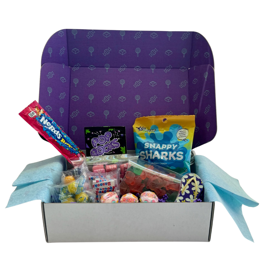 Open gift box filled with colorful candies and snacks, with purple interior decorated with geometric and lollipop patterns, and light blue tissue paper lining the edges.