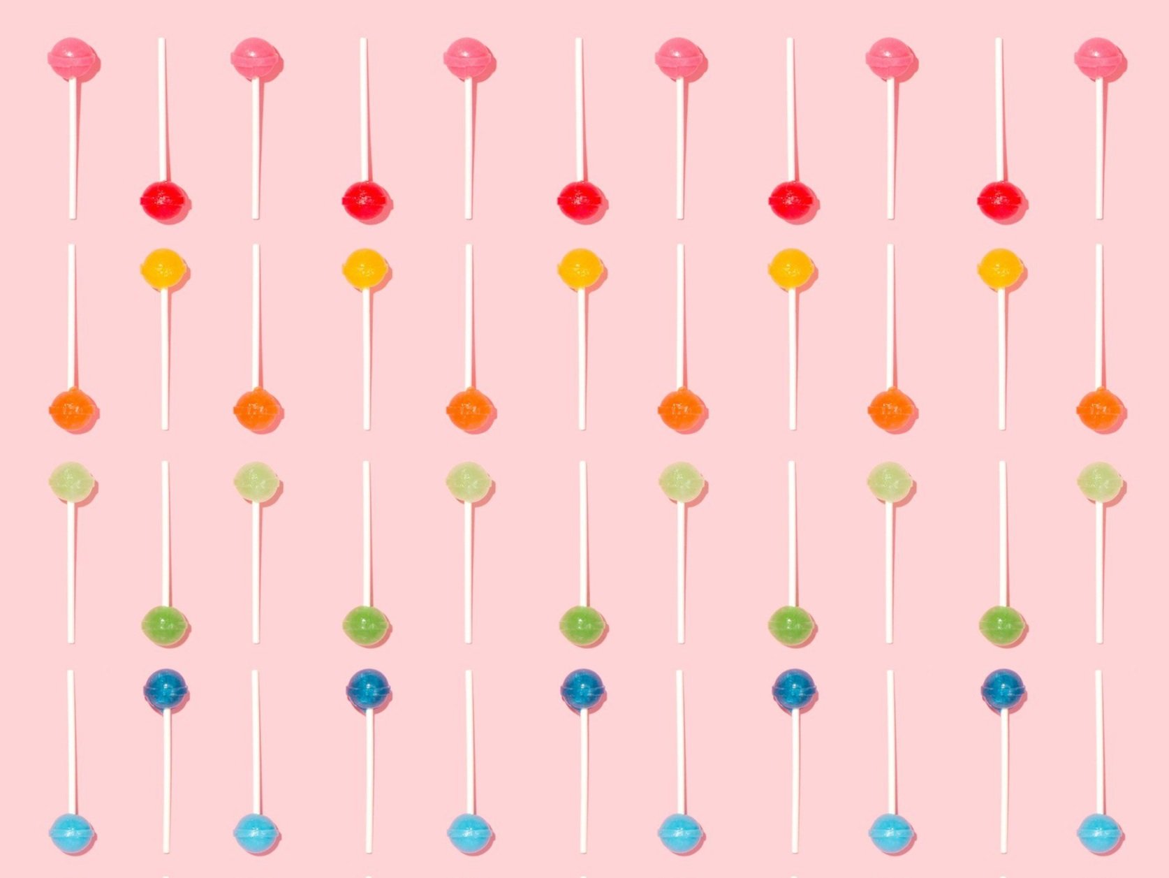Colorful lollipops arranged in rows on a pink background.