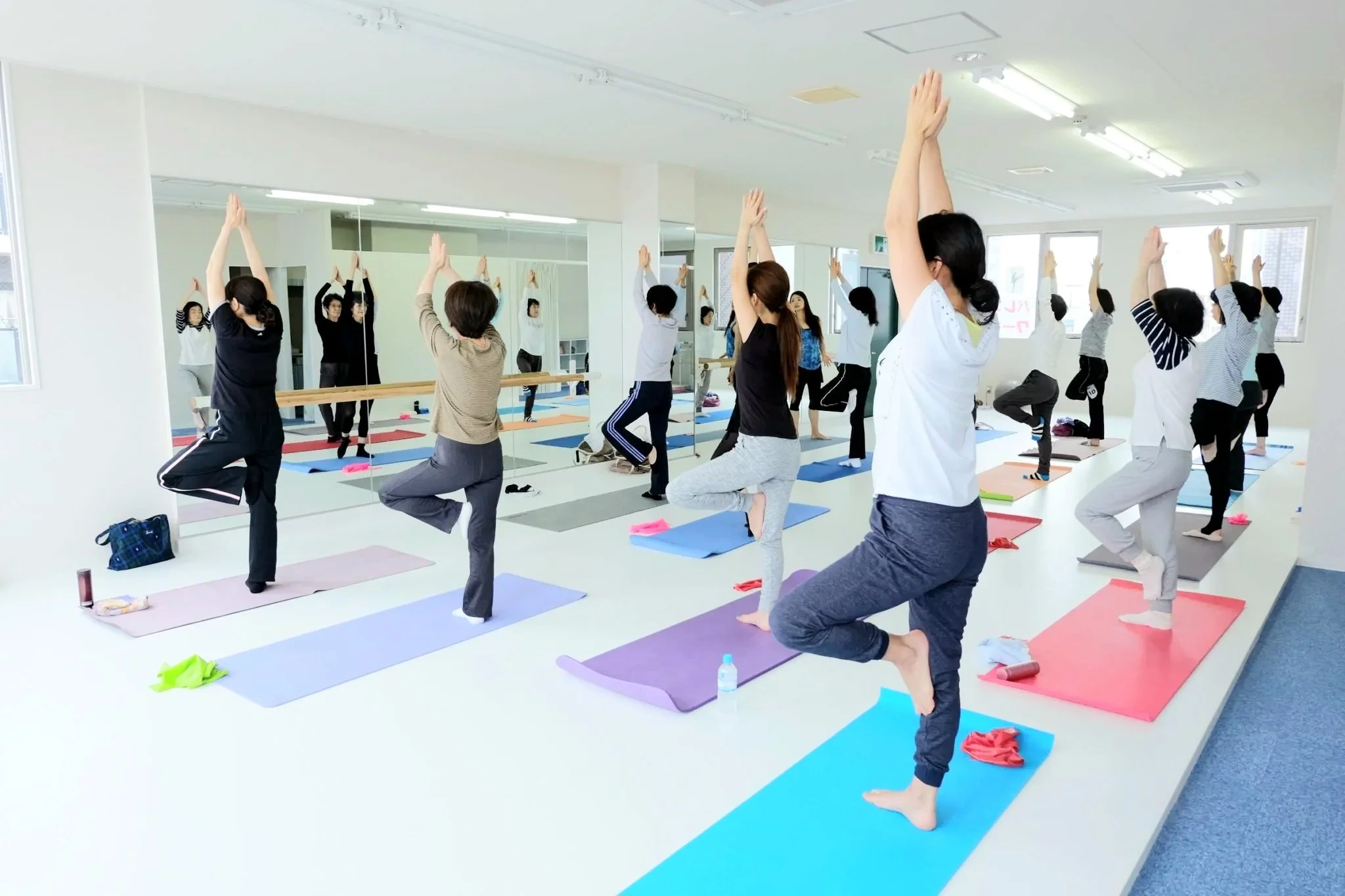 Lithe Life Studio Hako Body Tuning Class. A large group of women do the tree pose in a brightly lit studio with big mirrors.
