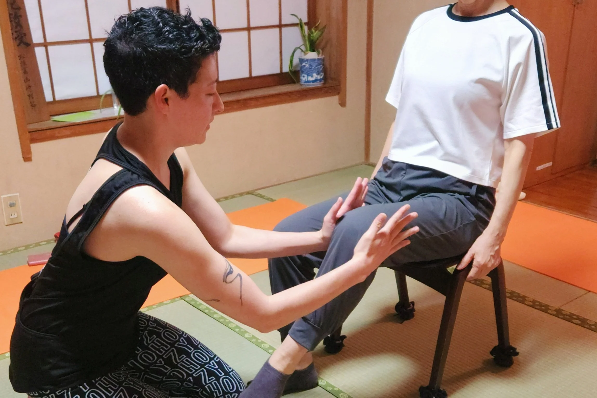 HOZY Consultation. Instructor helps client realign their knee and move their leg from inside the hip joint. Client is sitting on a chair in a tatami room.