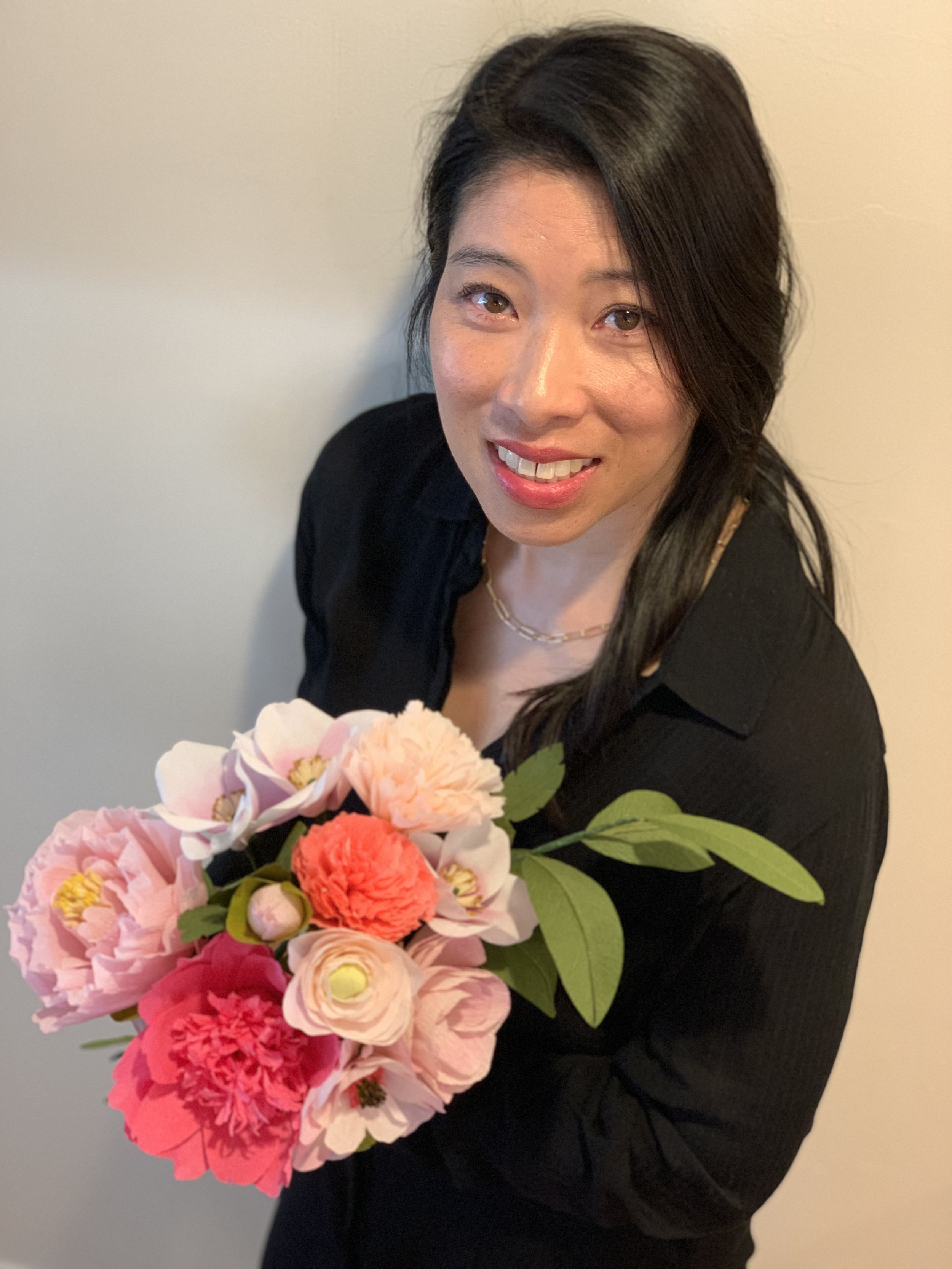 A woman with long dark hair smiling while holding a bouquet of pink and red flowers.