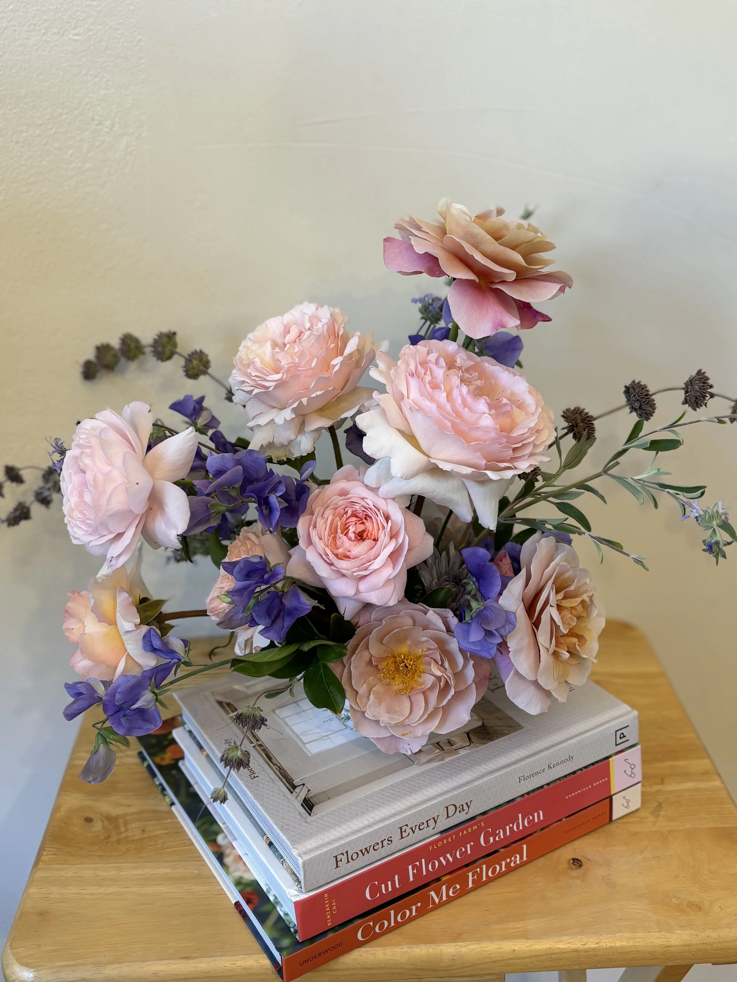 A bouquet of pink and purple flowers placed on top of a small stack of three gardening books on a wooden table.
