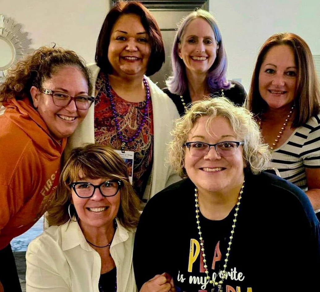 A group of seven women smiling indoors, posing for a photo together.