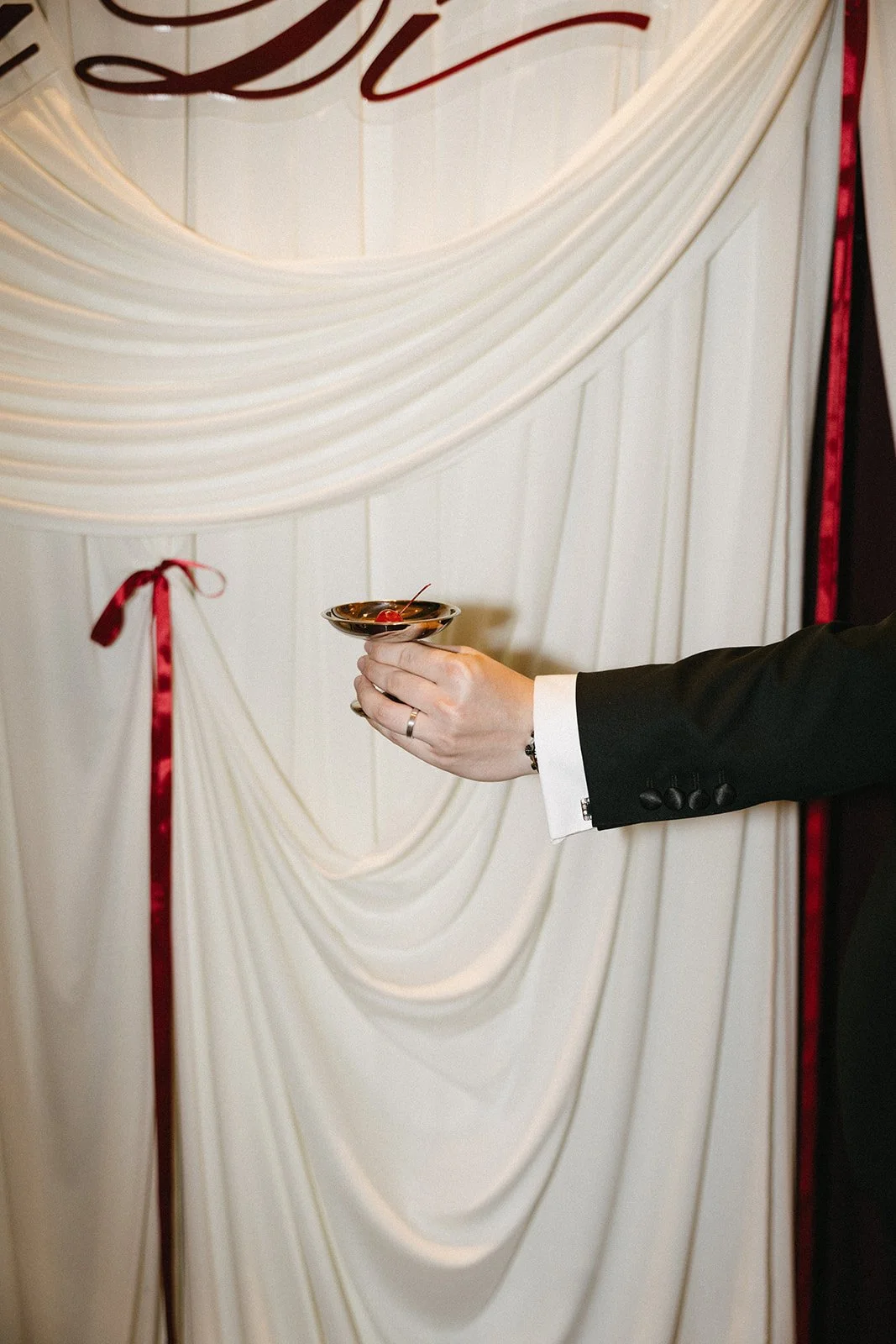 Minimalist ceremony backdrop with ivory fabric draping and red ribbon ties, captured during modern Asian wedding celebration