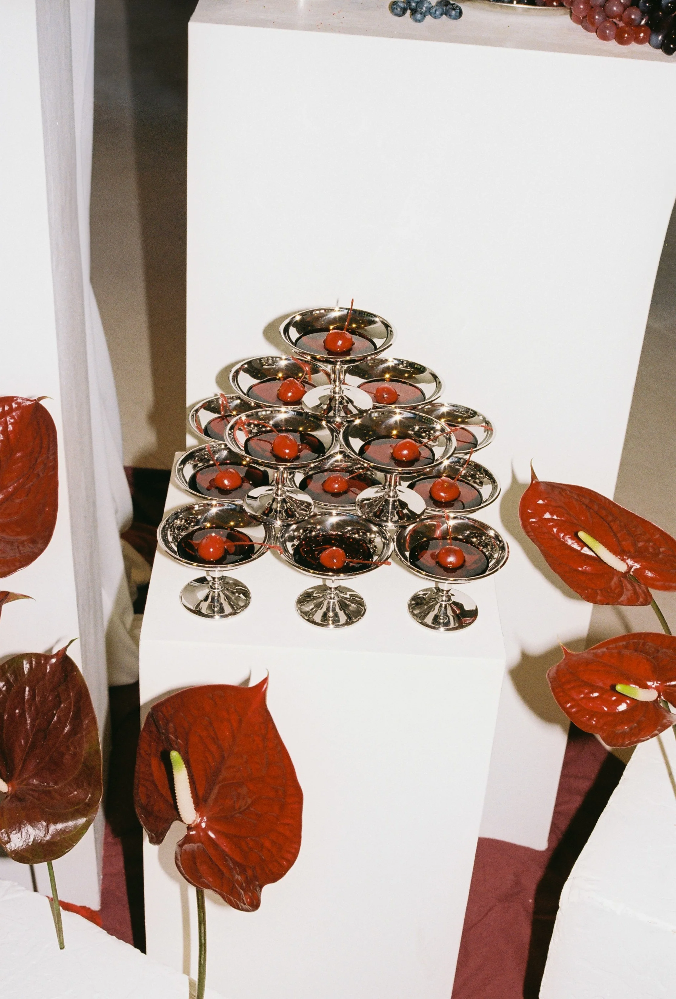 Contemporary champagne tower featuring red cherries in coupe glasses, styled with sculptural red anthuriums
