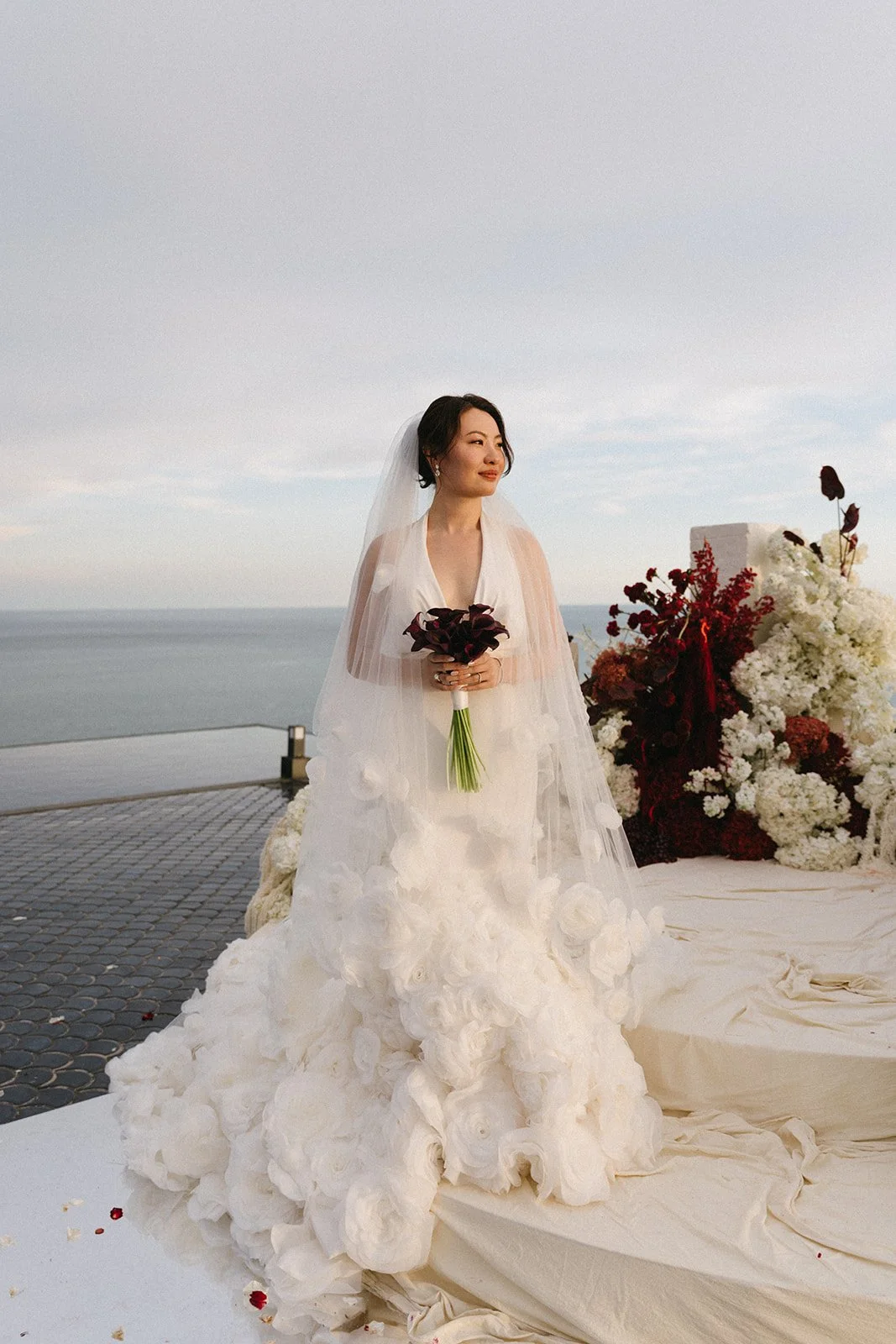 Bride standing in floral ceremony setup in wedding dress with ocean views in Phuke