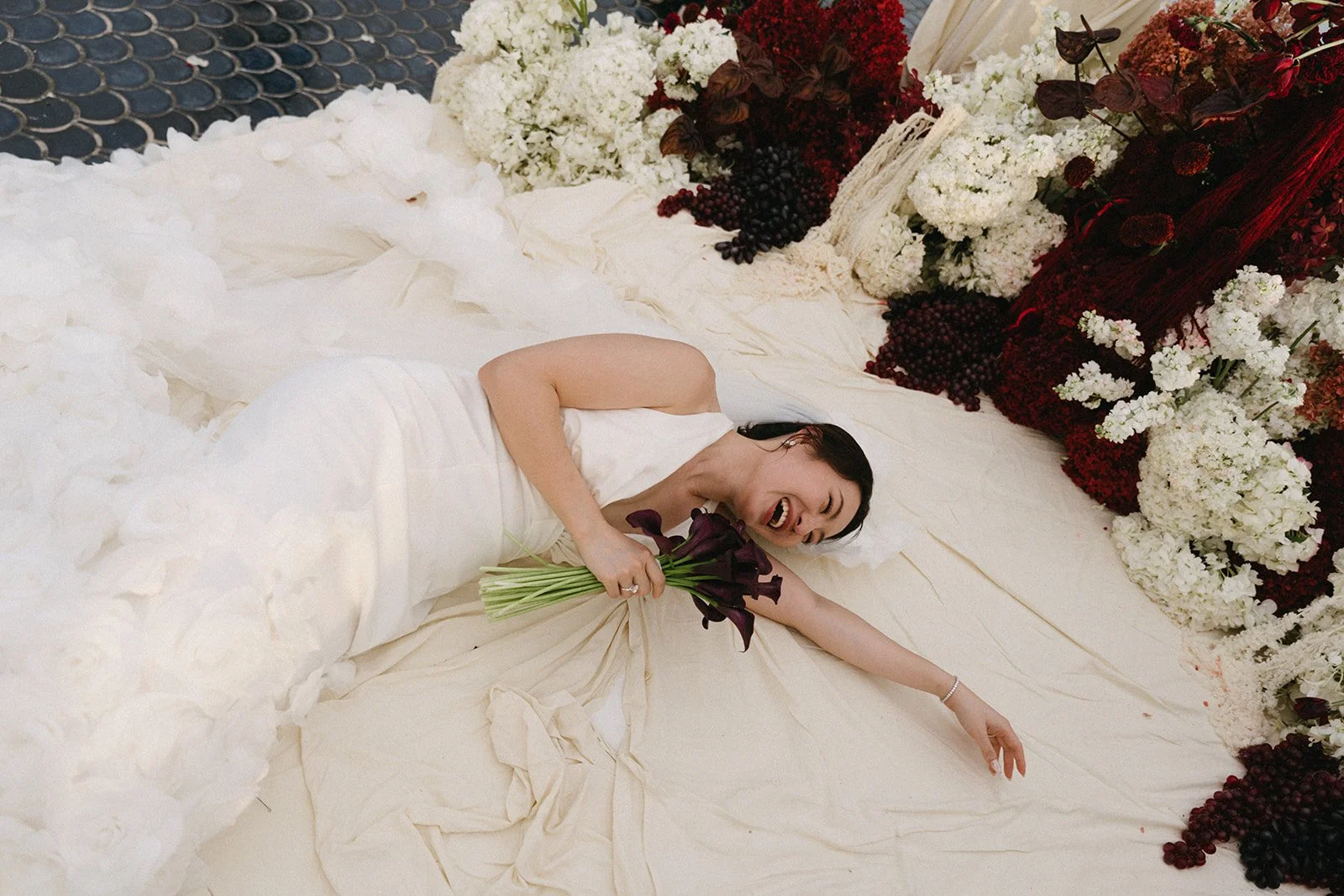Bride in wedding gown lying on ceremony platform surrounded by red and white florals at Sri Panwa wedding in Phuket