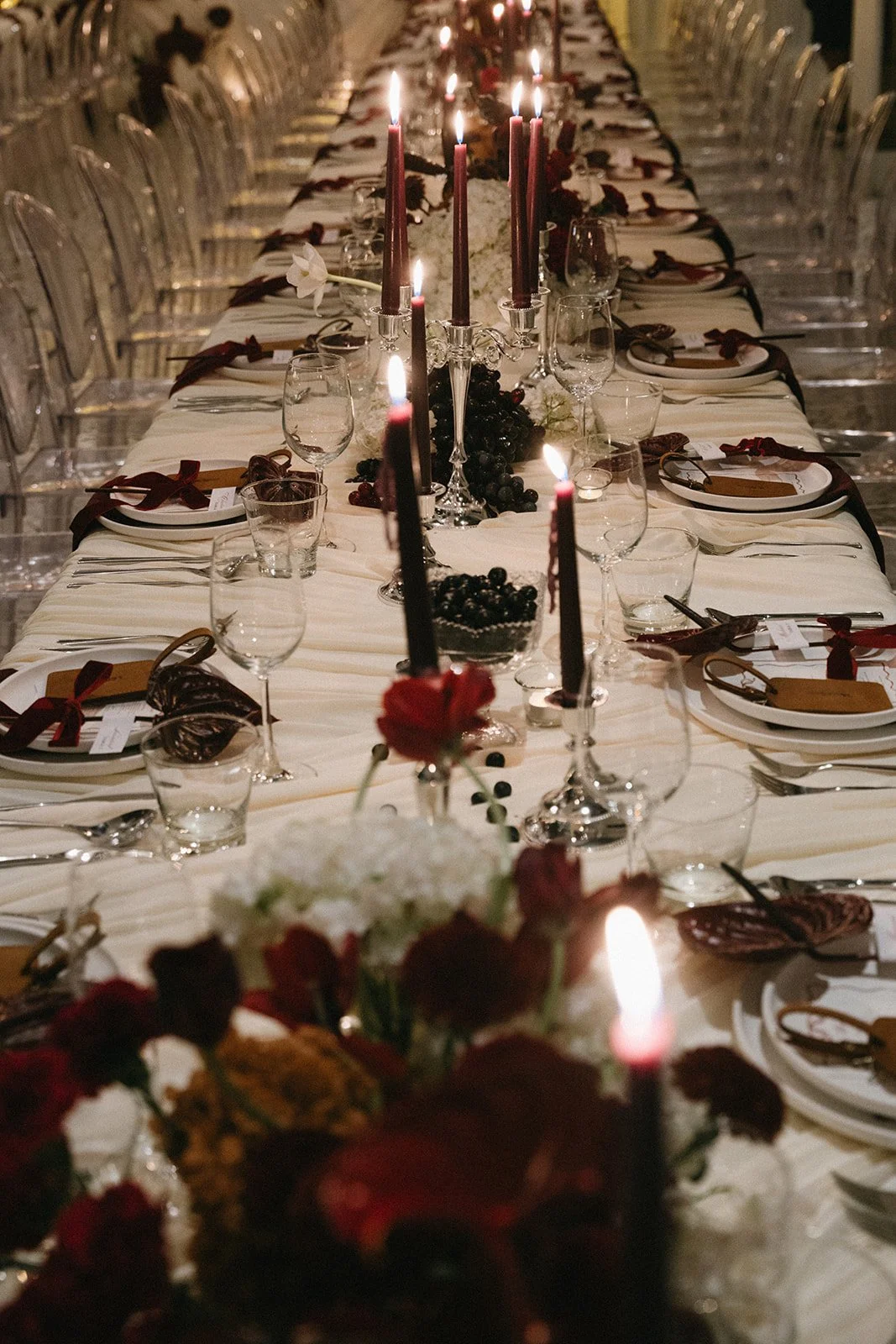 Long wedding reception table with candlelight, red and plum florals, and black dinnerware at destination wedding in Thailand