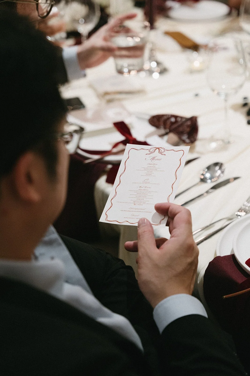 Guest holding handwritten place card with red ribbon at intimate Sri Panwa wedding reception