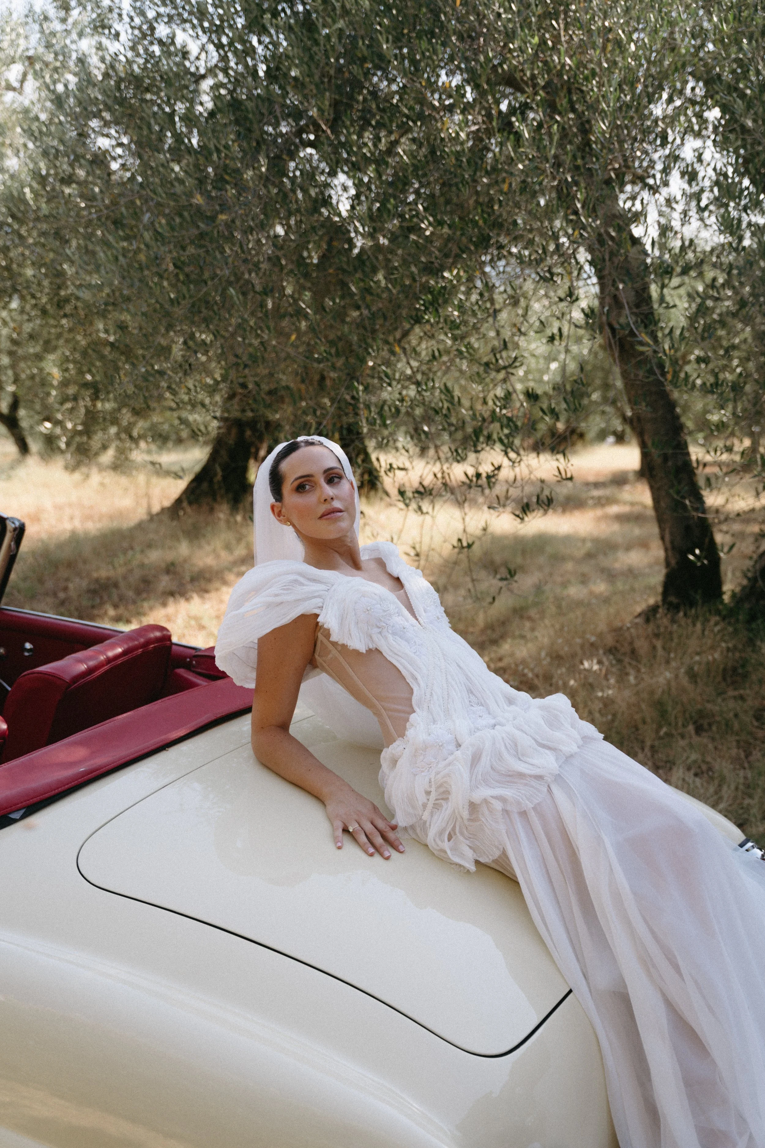 bride sitting on vintage car wearing rara avis gabriella gown