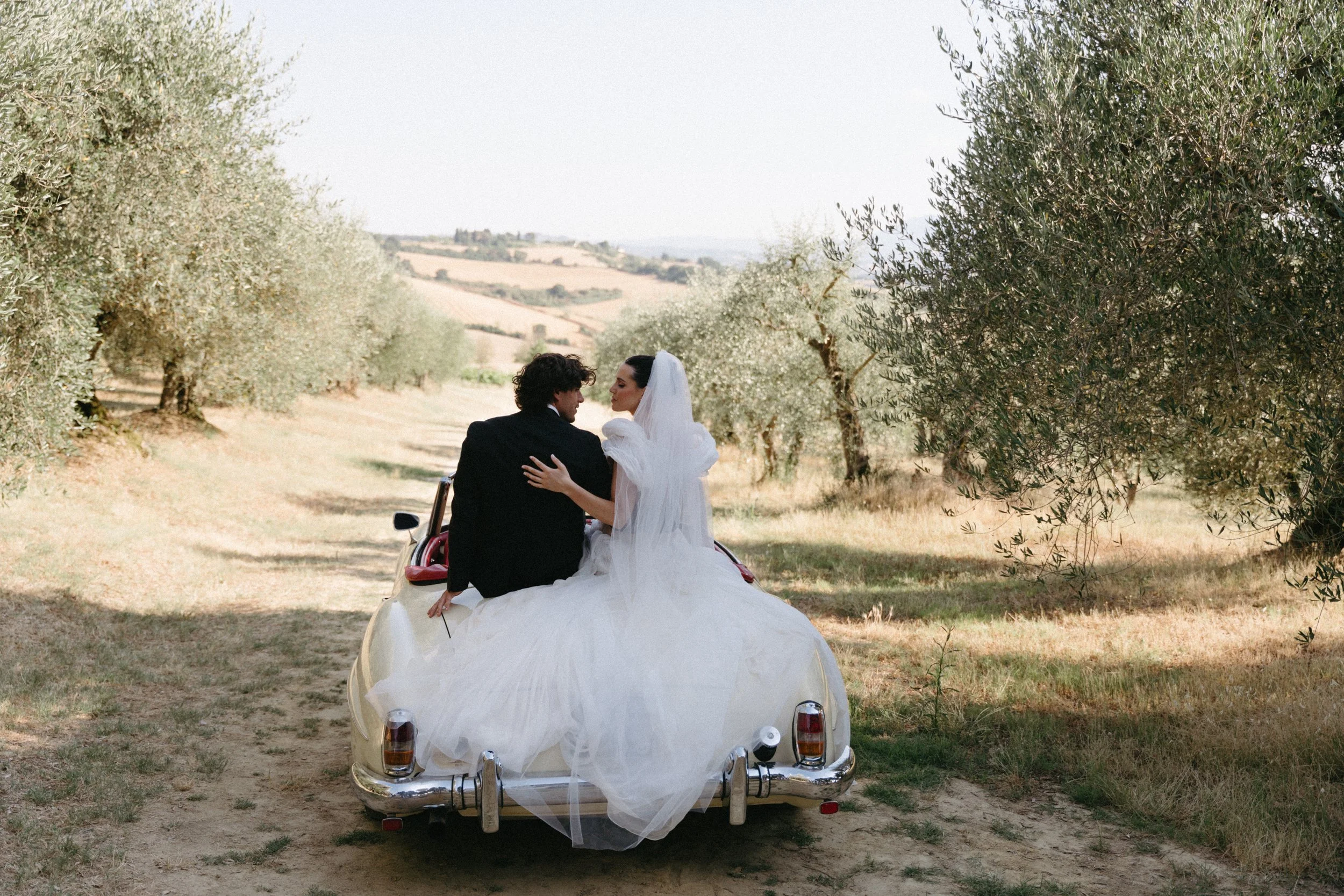couple sitting in vintage car bride fixing makeup in car window at Villa Cozzano Tuscany wedding editorial