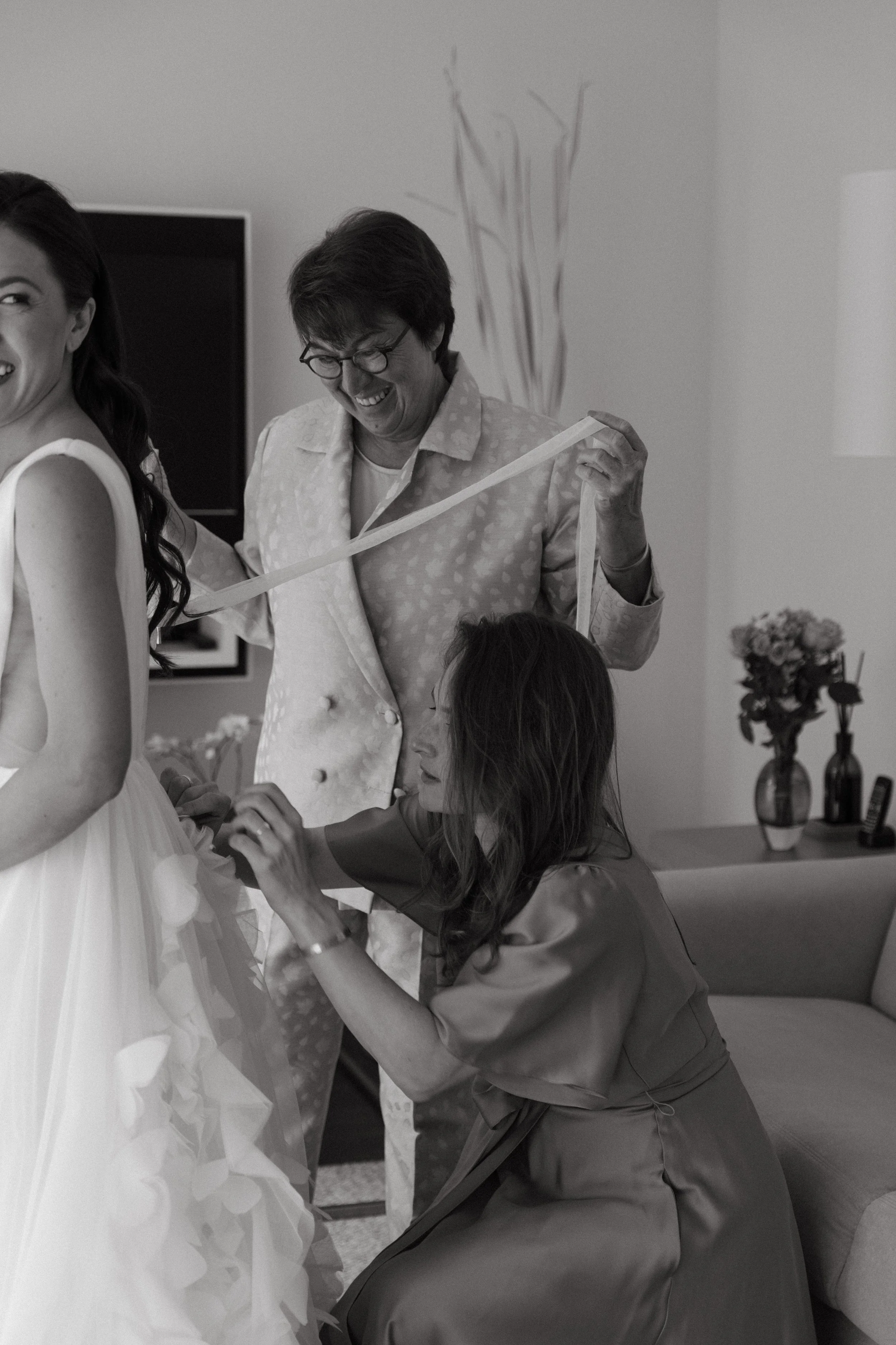bride's mum and friend helping her tie her wedding dress