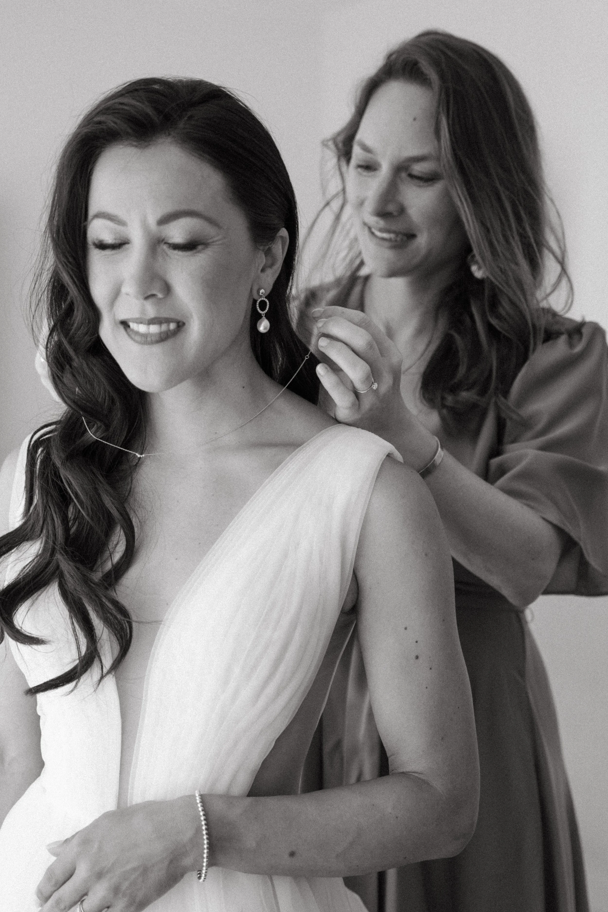 bride's friend putting on her necklace as she gets ready for wedding ceremony
