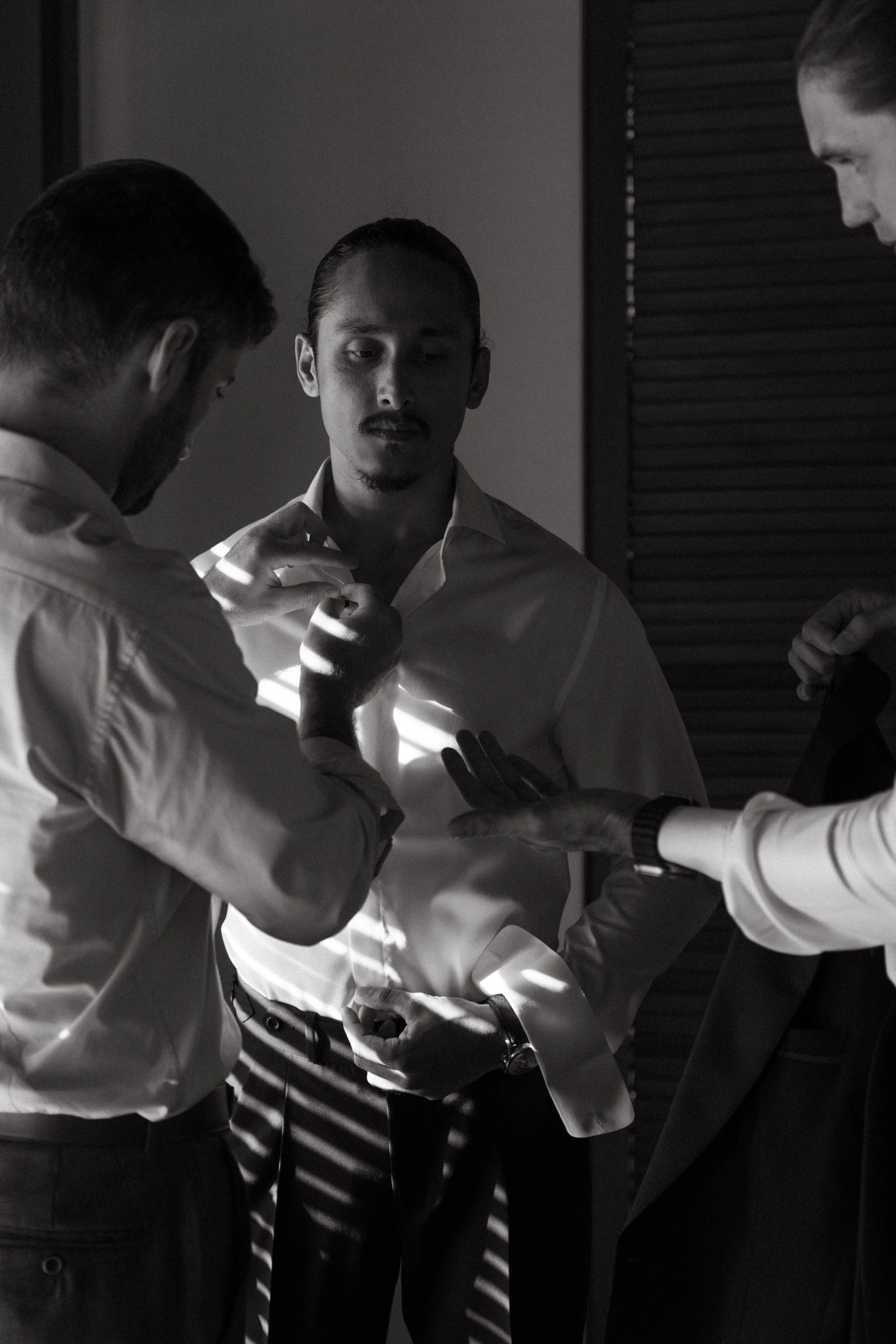 black and white portrait of groomsmen helping groom with bow tie during preparations
