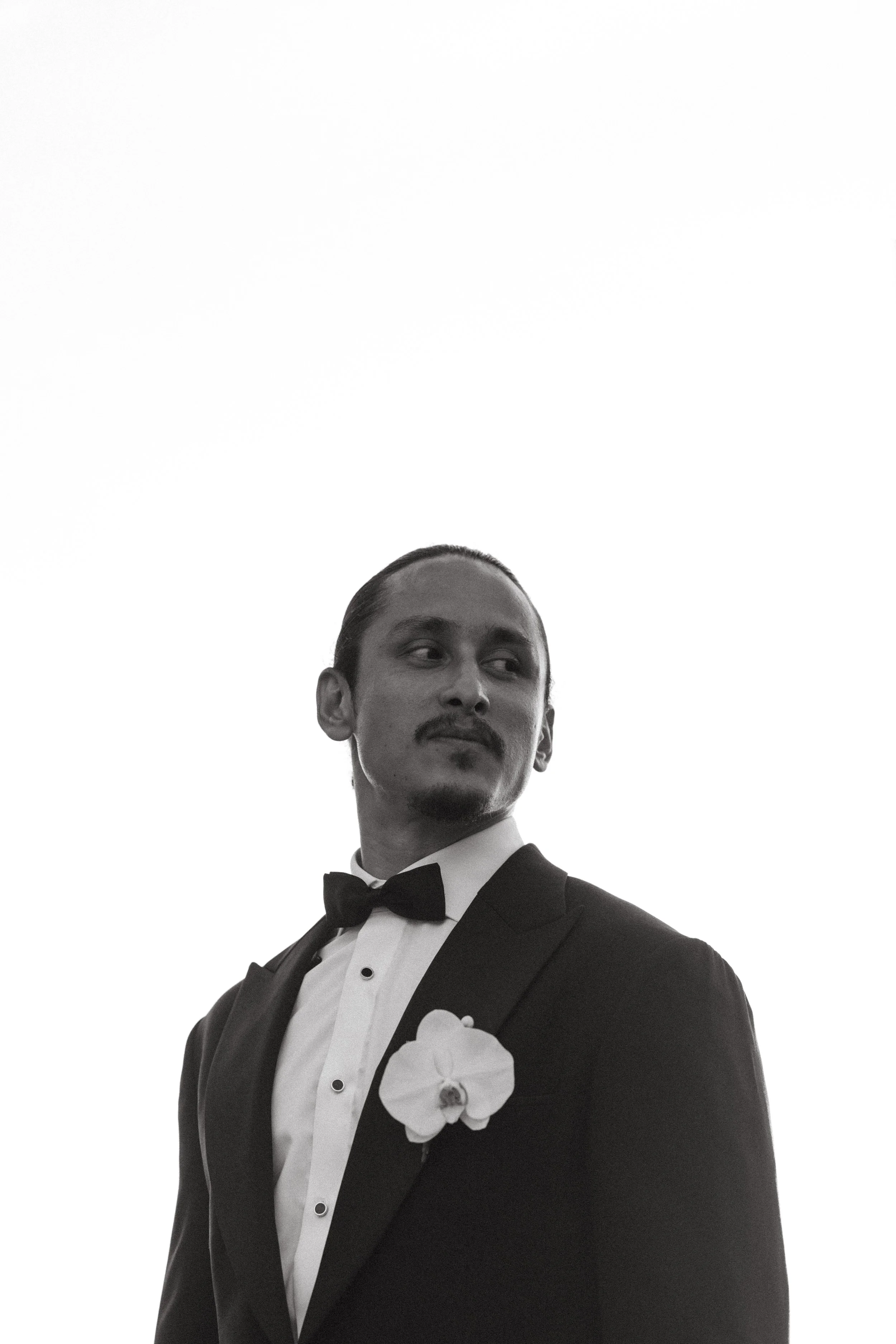 black and white portrait of groom wearing tux with an orchid button hole piece