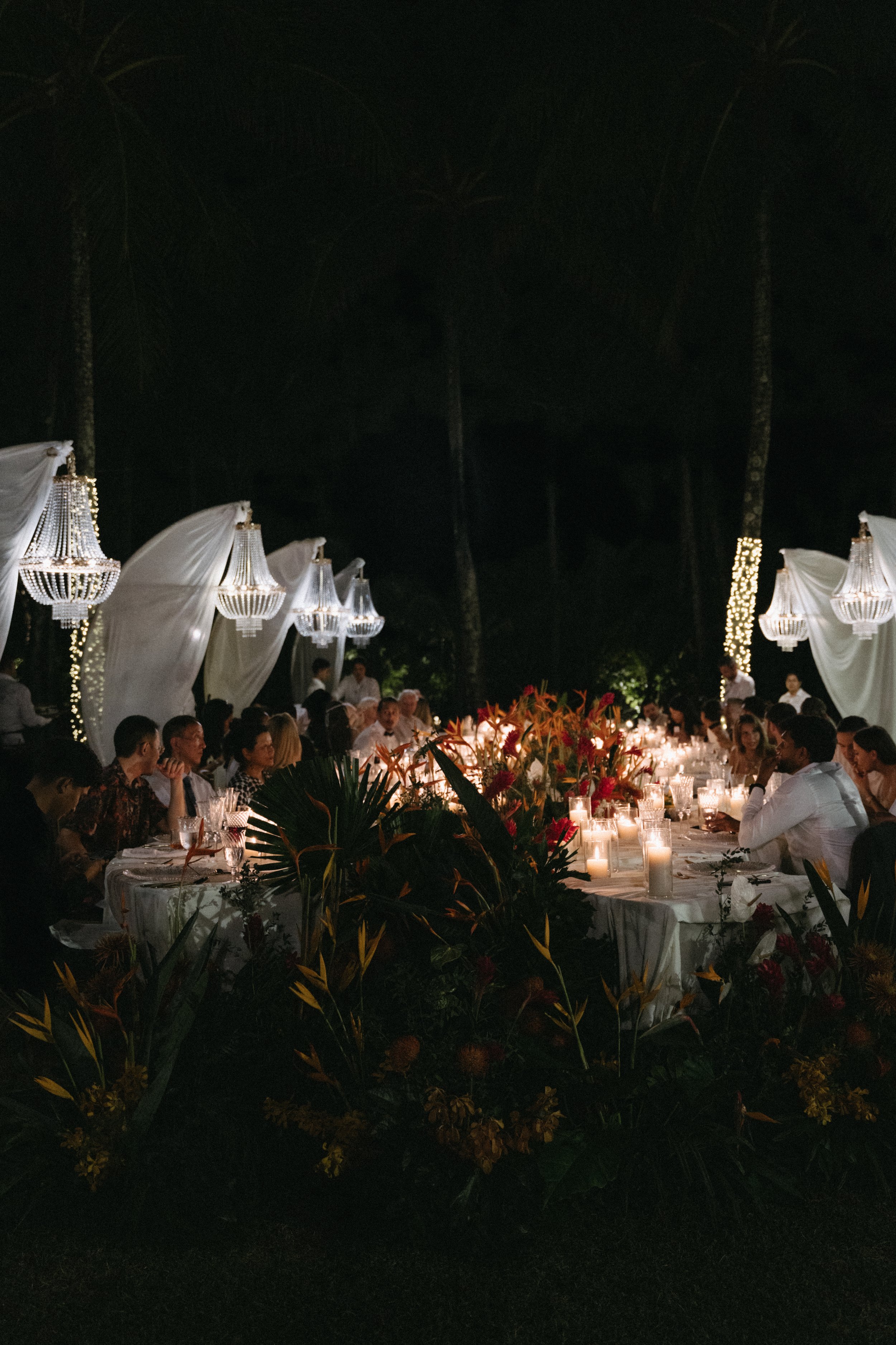 stunning outdoor wedding reception setup illuminated by candles and outdoor chandeliers during the night