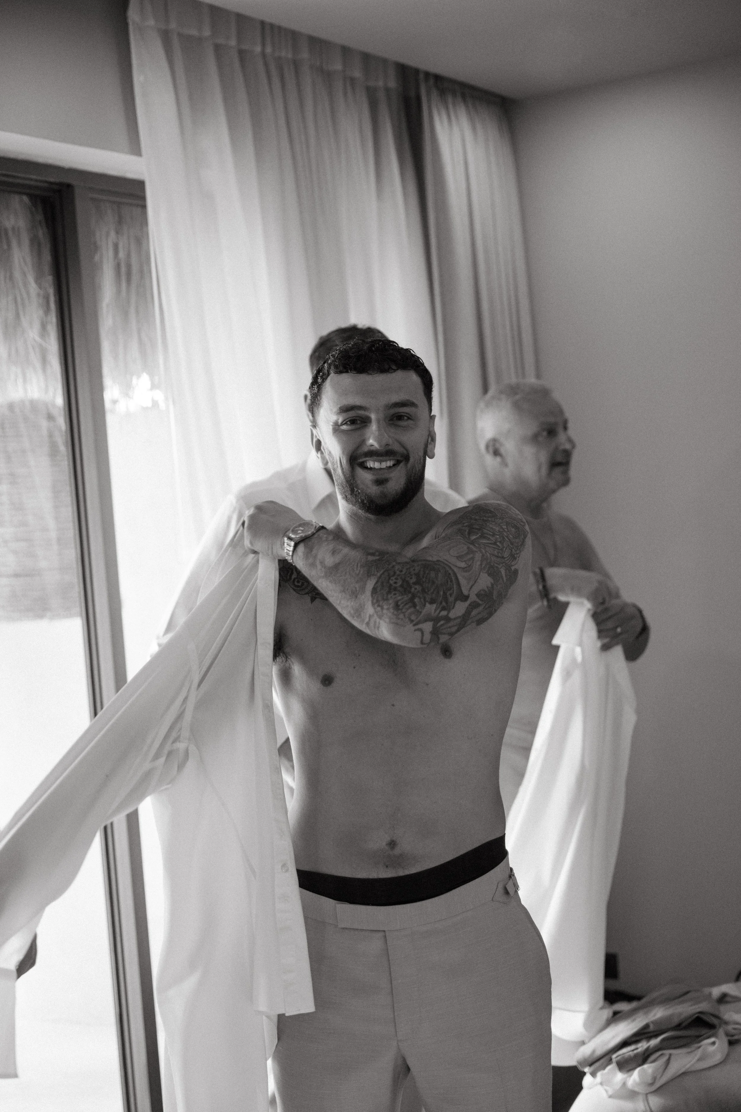 candid shot of groom putting on his shirt before wedding ceremony at odyssey mansion koh samui