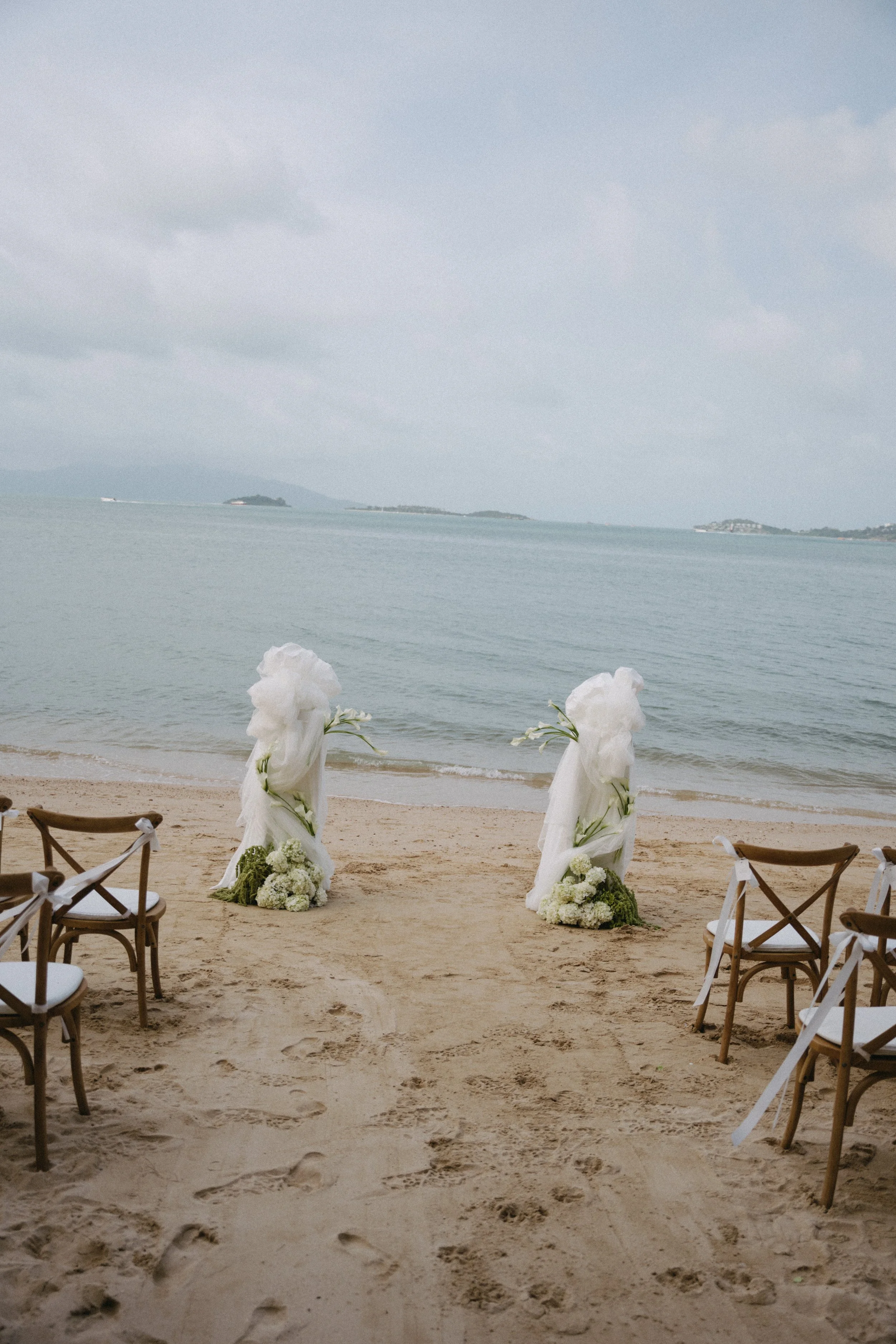 Wide view of a destination wedding ceremony on Bangrak Beach in front of Odyssey Mansion, Koh Samui, with ocean views and floral installations