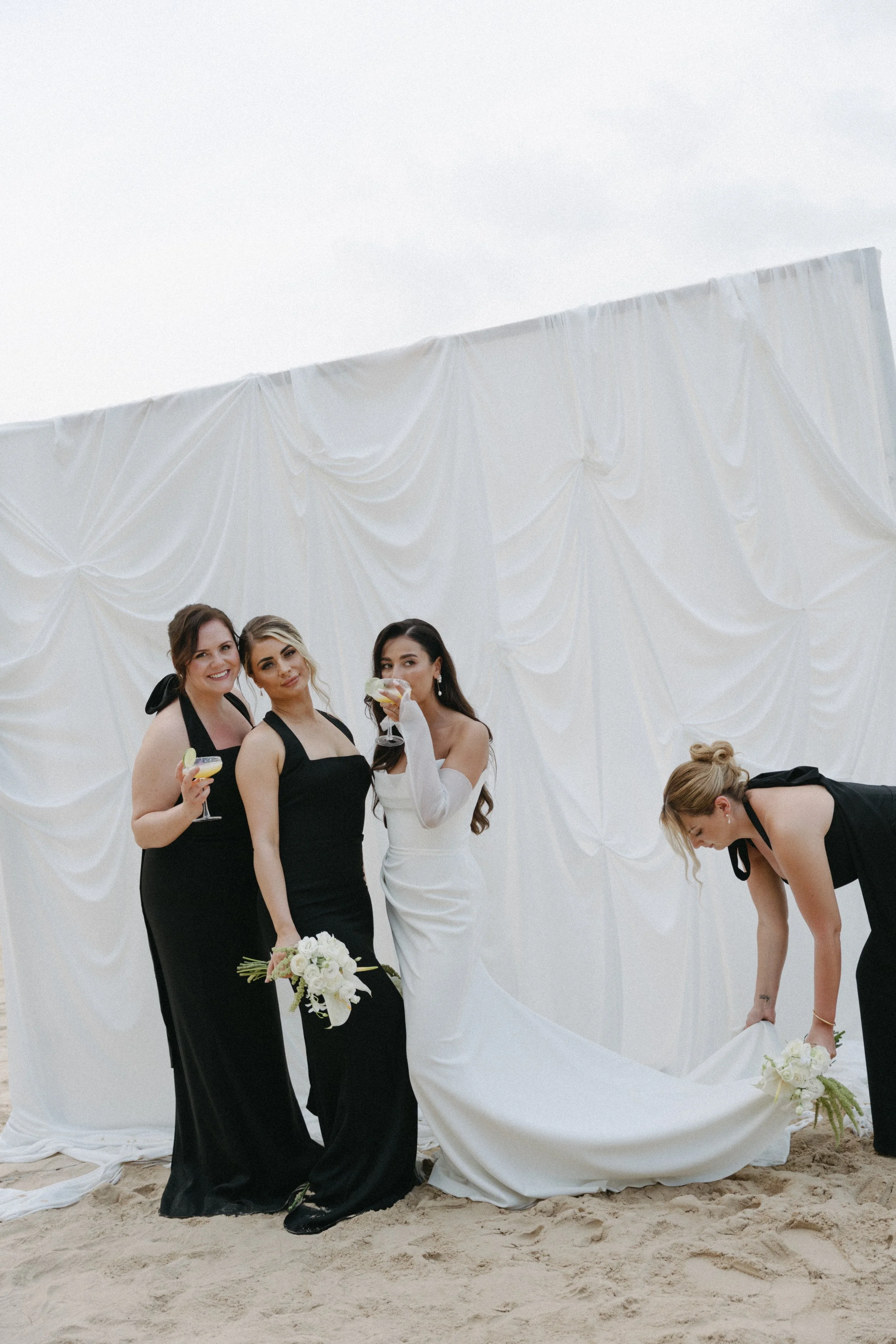 bride enjoying cocktails with bridal party as maid of honour fixes her train