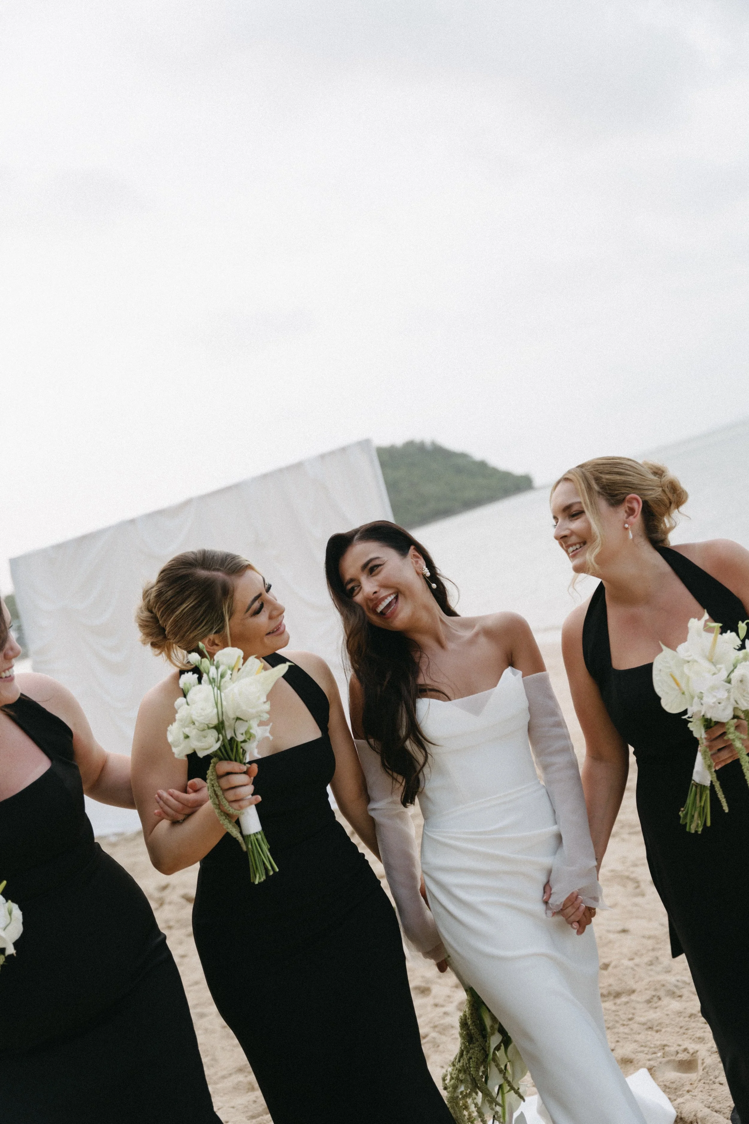 documentary style shot of bride with bridesmaids walking along the beach after wedding ceremony