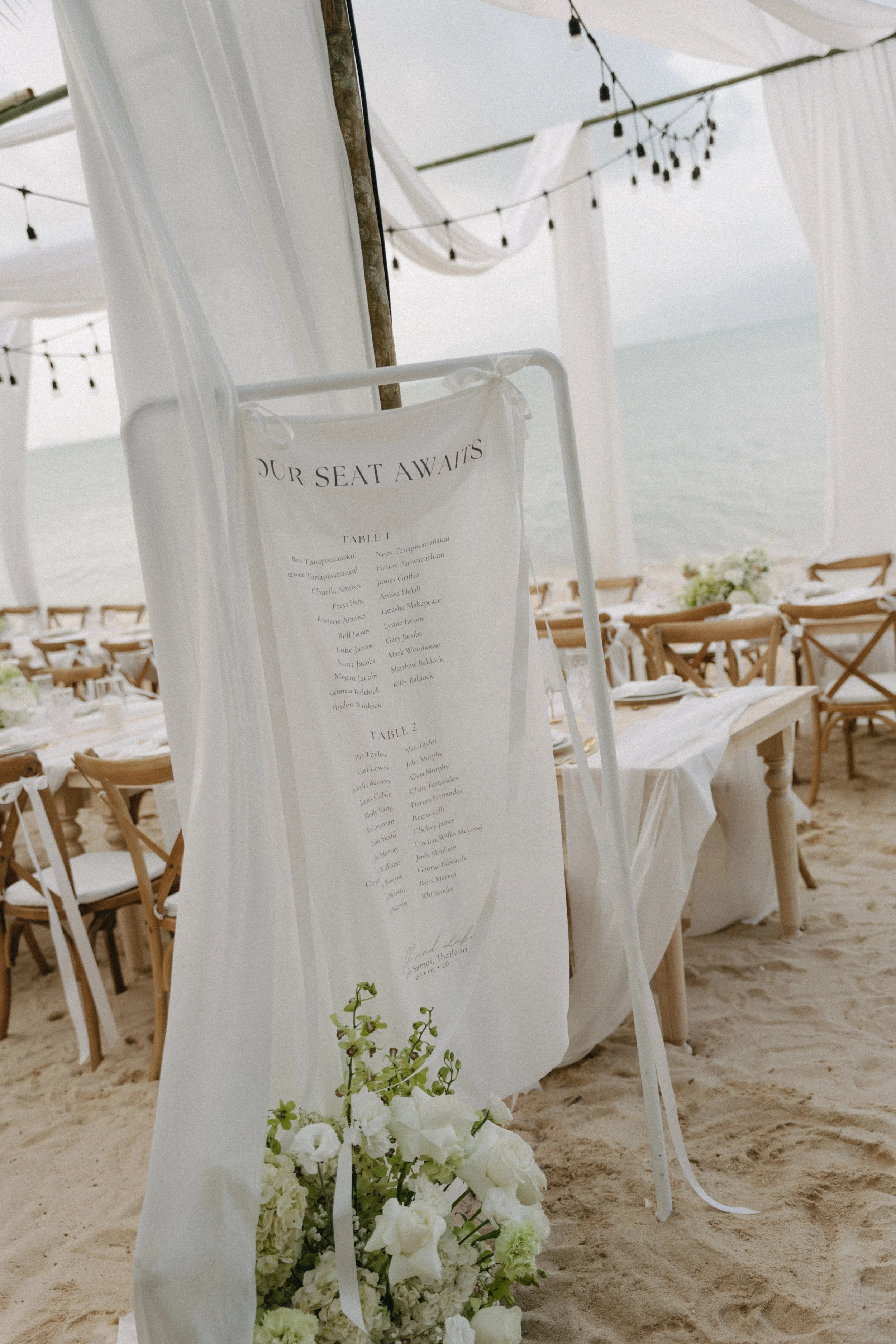Outdoor wedding reception seating chart display draped in white fabric on Bangrak Beach, Koh Samui