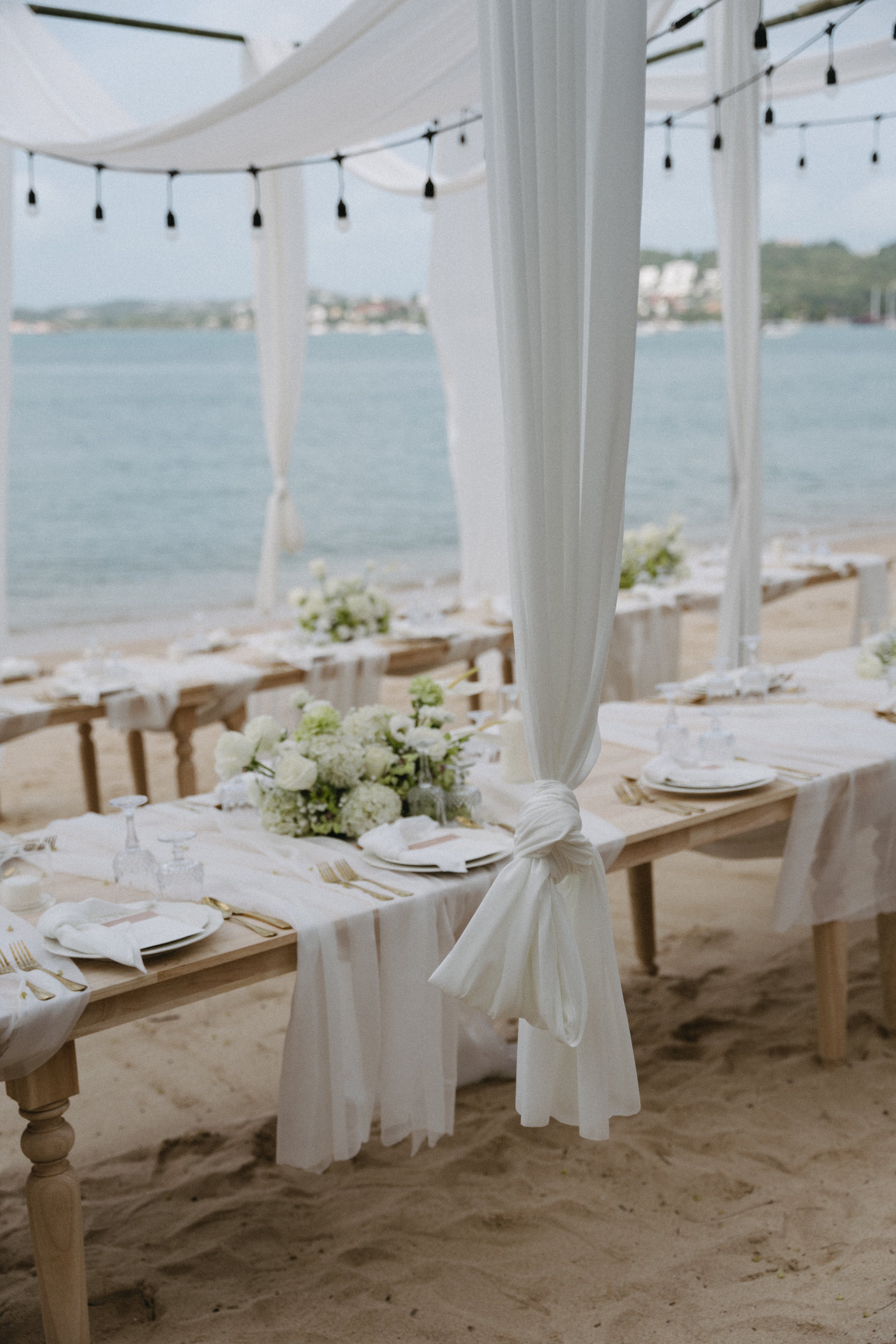 Beachside wedding reception table under white canopy with fairy lights at Bangrak Beach, Koh Samui