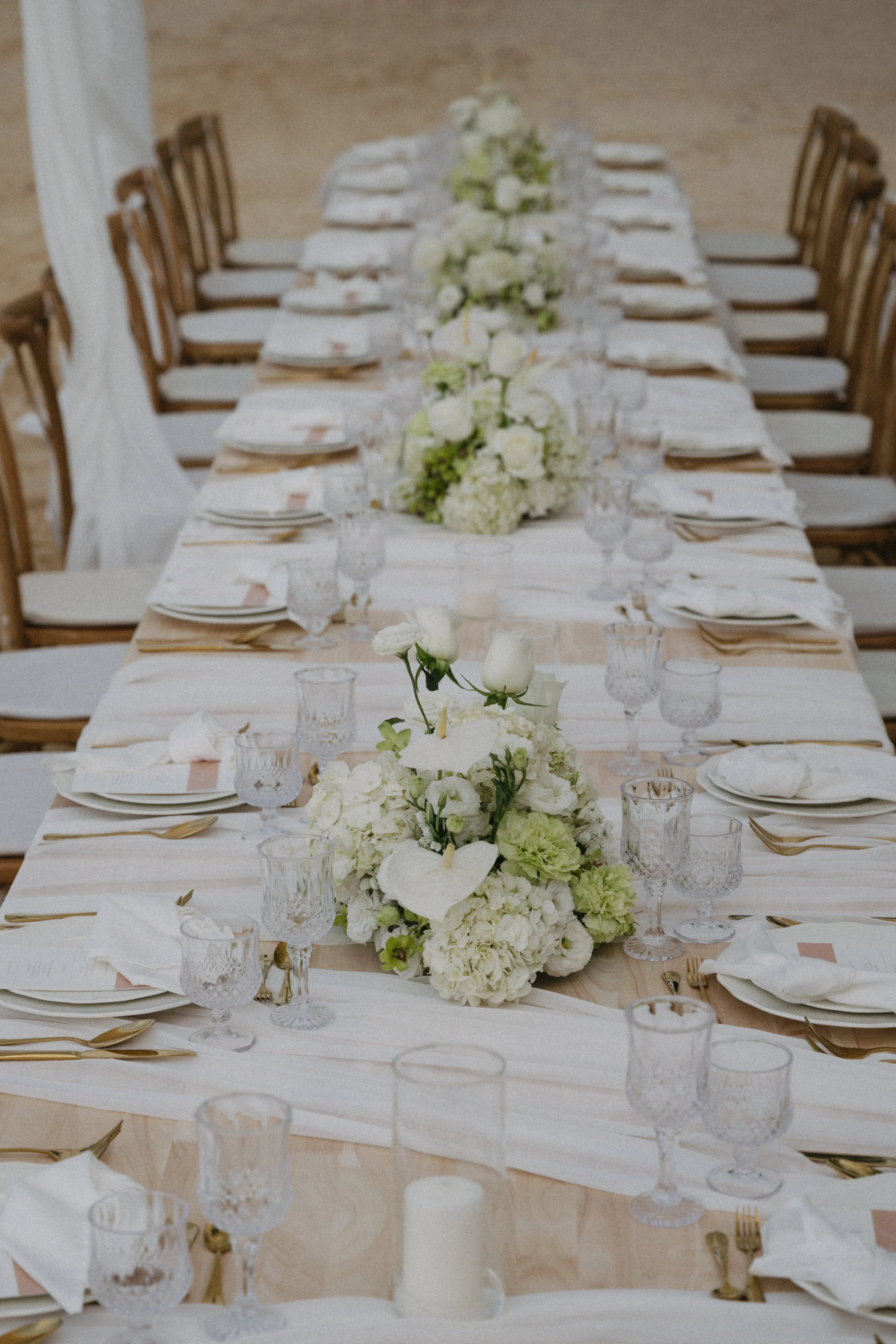 Styled long reception table with white linen, glassware and white floral centrepieces for a luxury beach wedding at Odyssey Mansion, Koh Samui