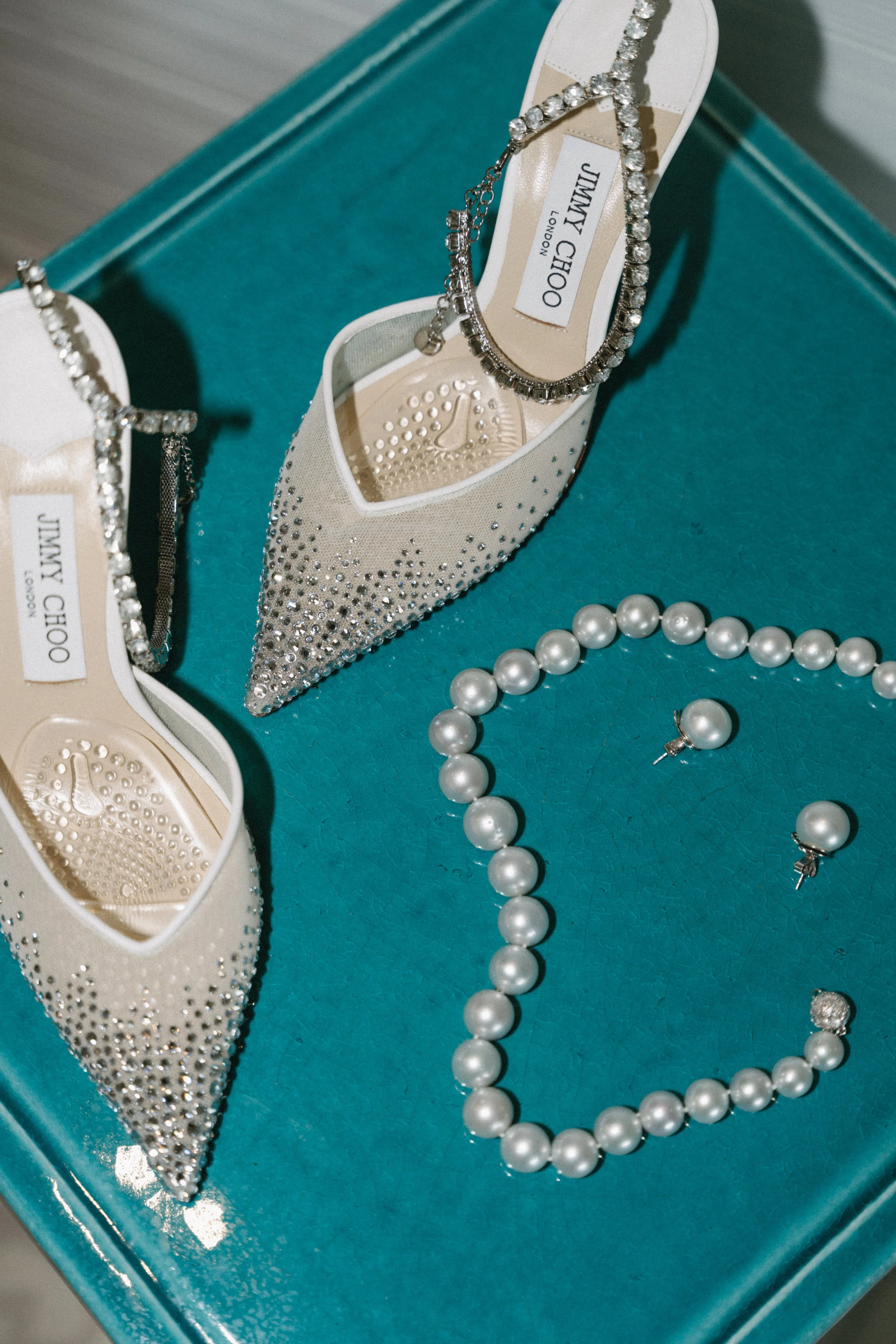 jimmy choo bridal heels and pearl necklace styled on teal table at COMO Point Yamu, Phuket wedding details flat lay