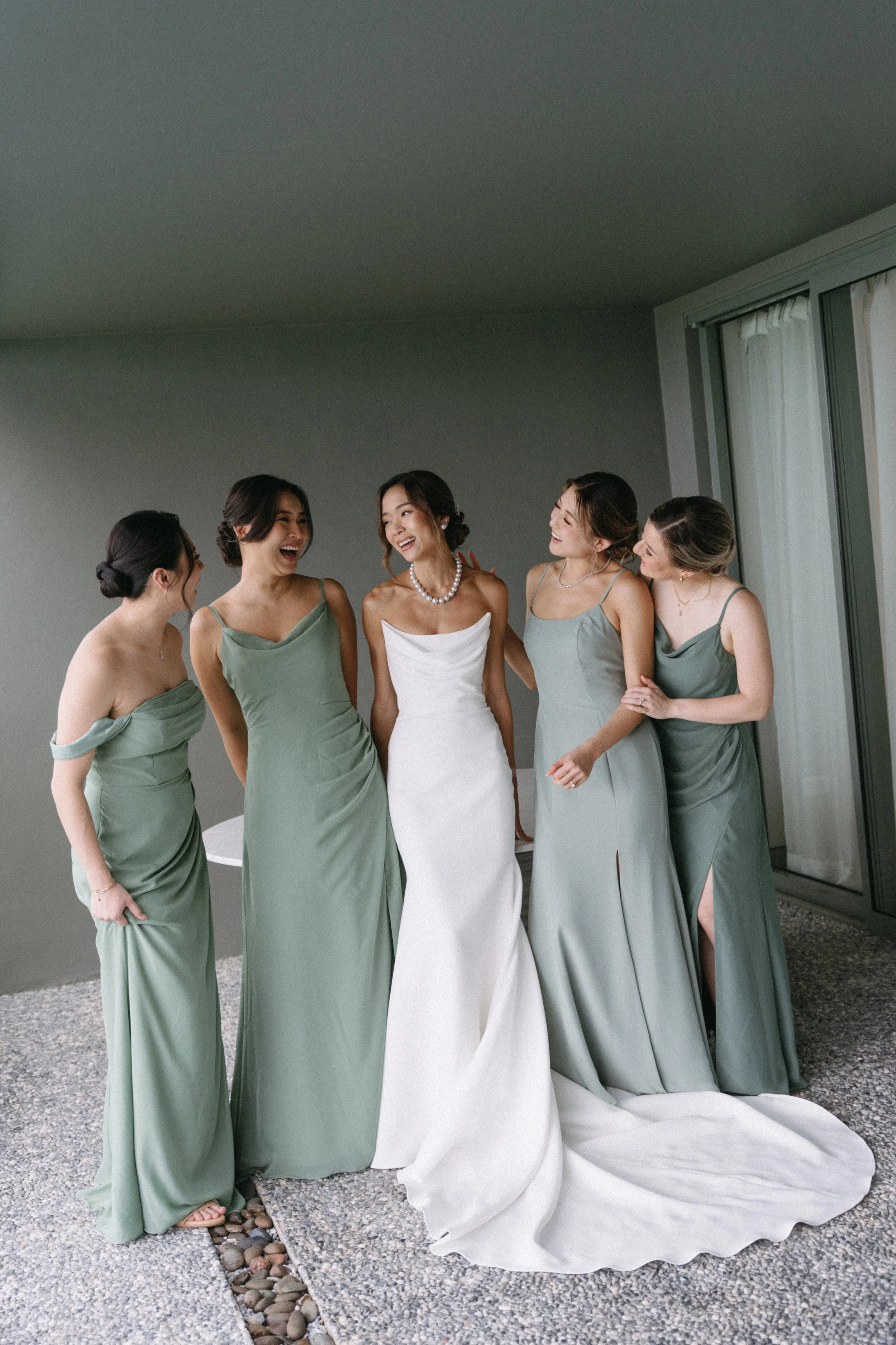 Bridesmaids in sage green gowns standing with bride in alex perry wedding dress