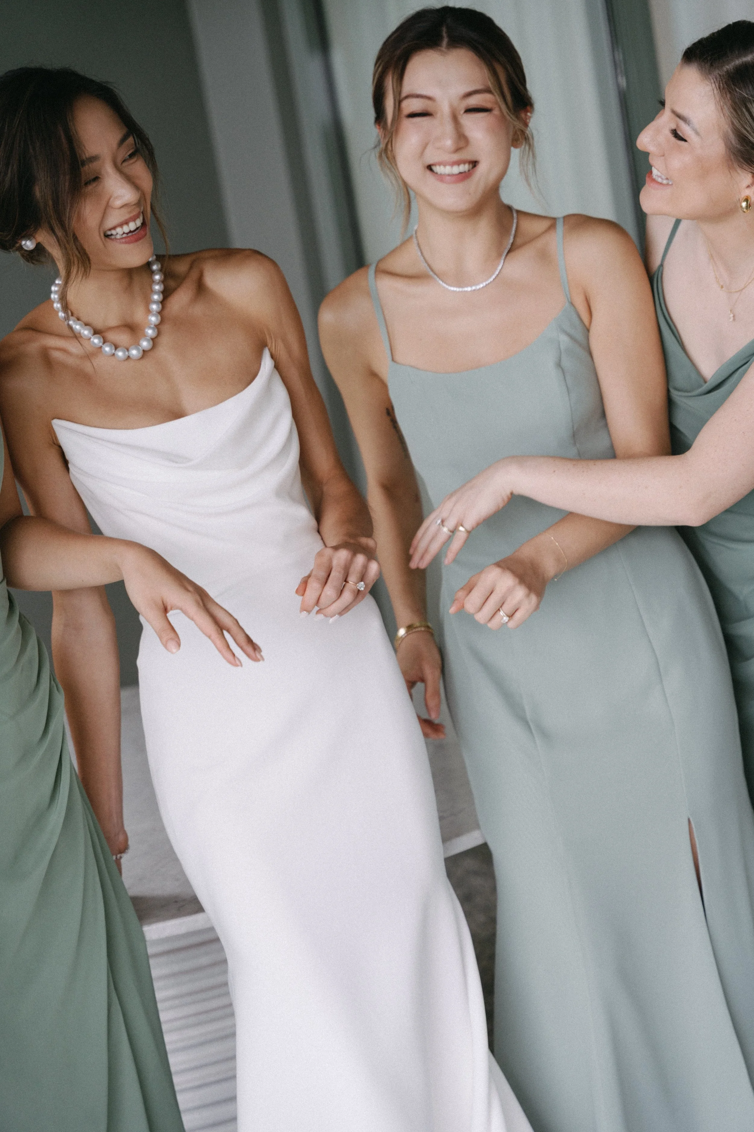 Bride and bridesmaids in sage green dresses laughing together, candid Phuket wedding party portrait