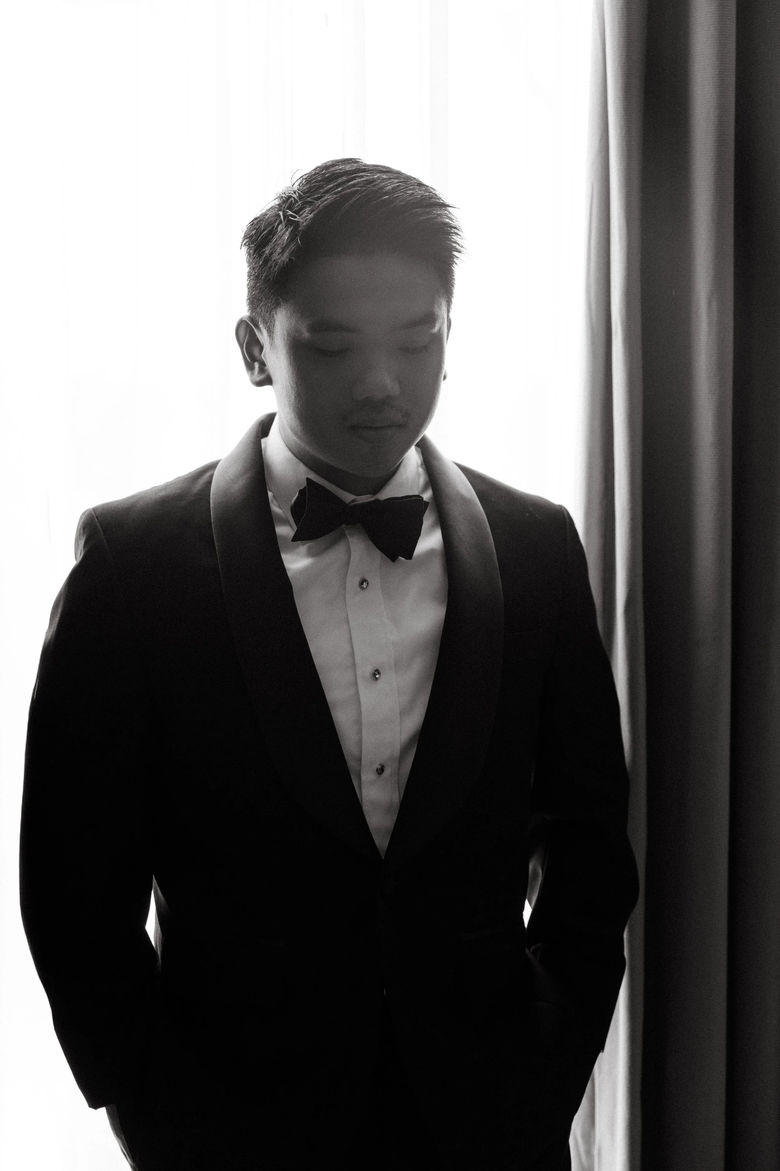Silhouette portrait of groom in black tuxedo and bow tie, moody black and white wedding photography