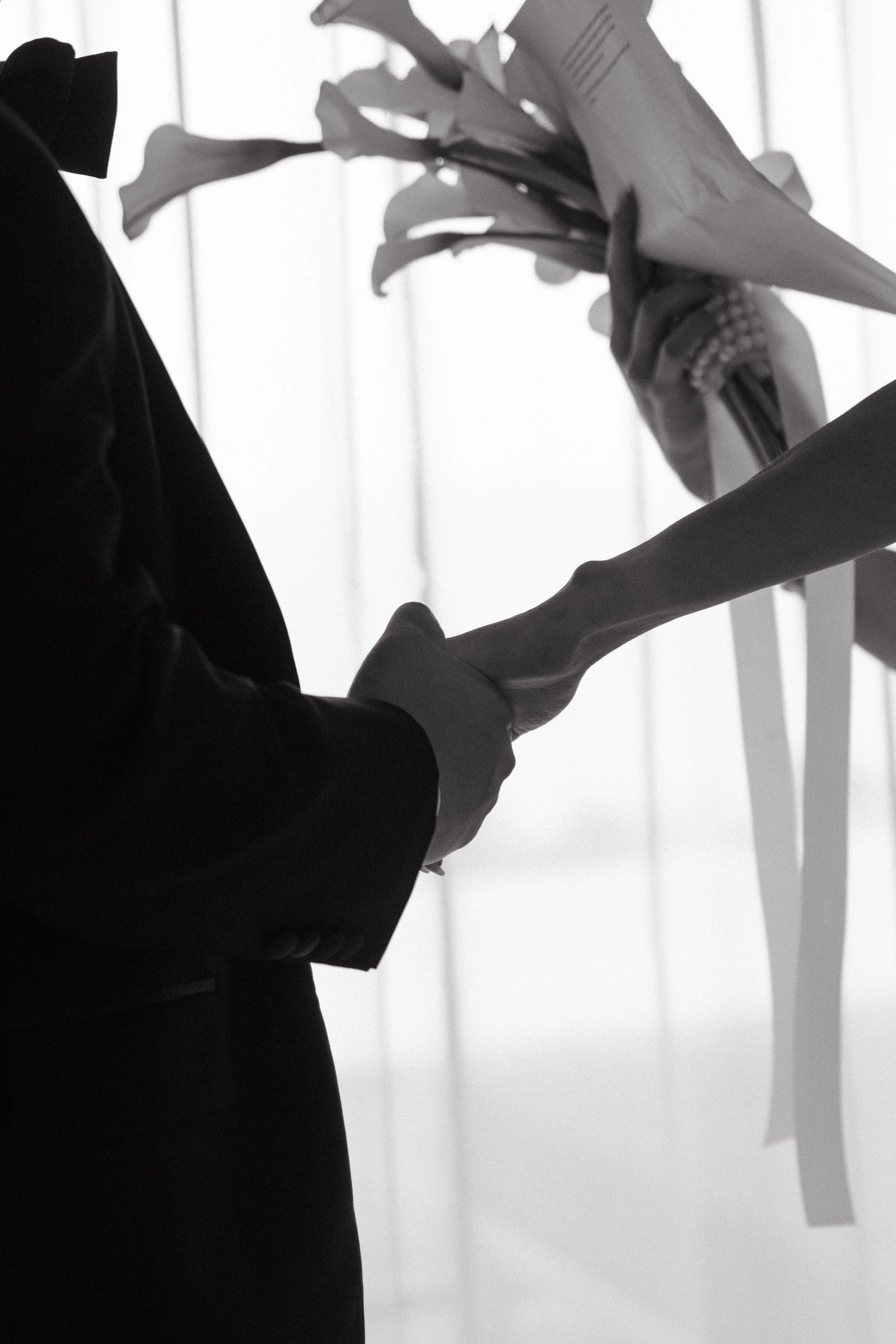 Close-up of bride and groom's hands during private vow exchange, calla lily bouquet detail